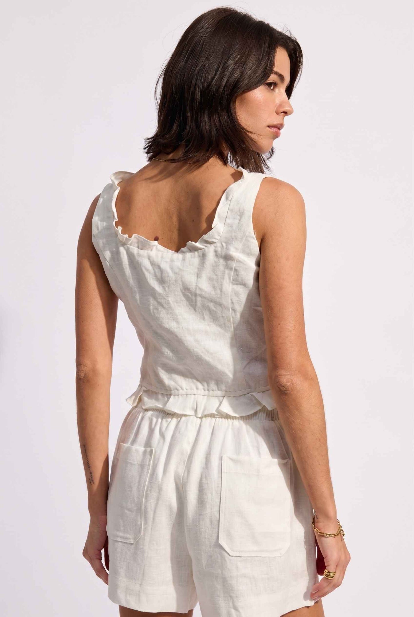 Model wearing Shay Ruffle Button-Front Top Cotton-Linen Tank Top in Off White with matching smocked shorts and heeled sandals