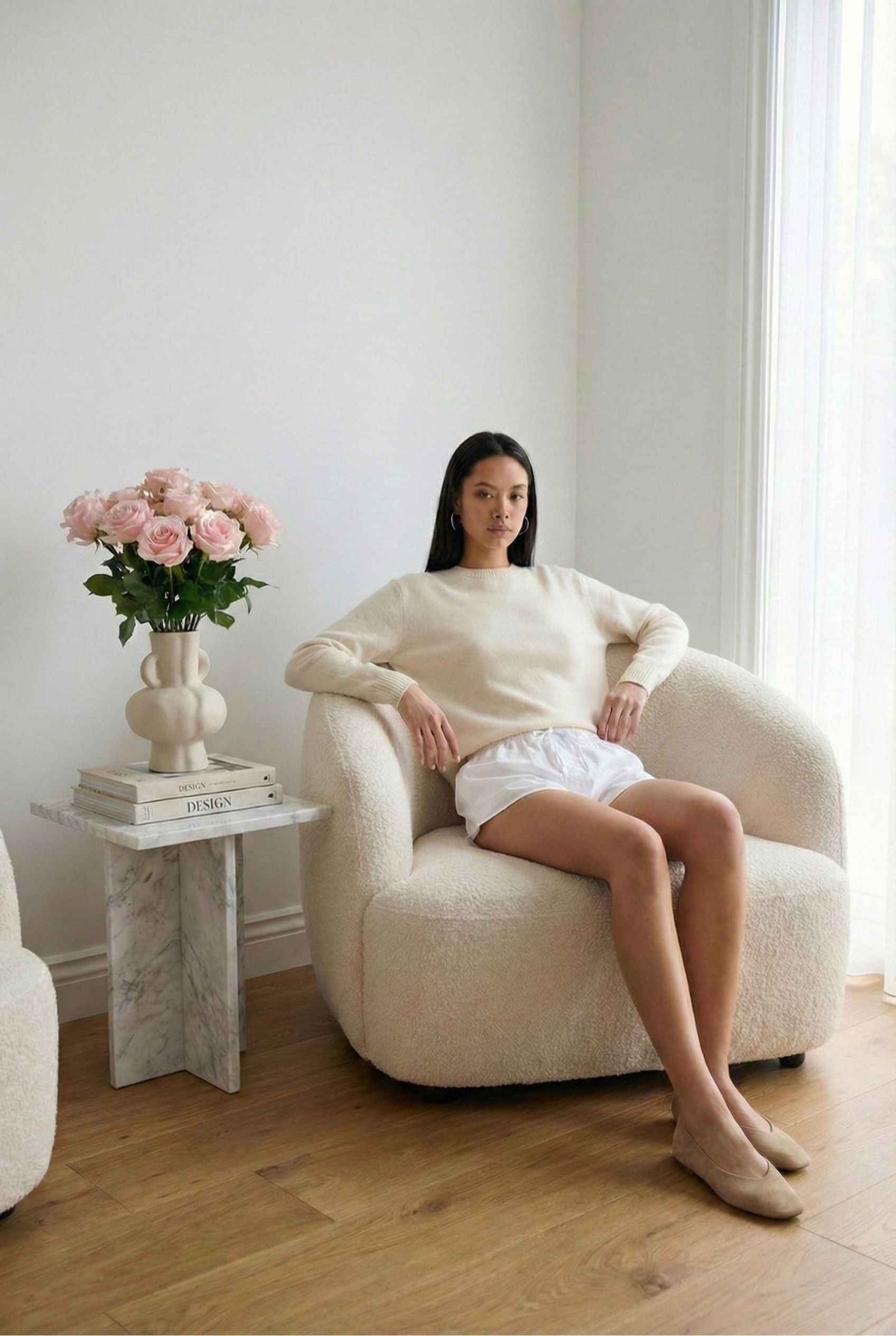 Model wearing Shea Skort in White Cotton-Blend Poplin Mini Skort with Drawstring paired with knit sweater and flats posing in feminine minimalist living room