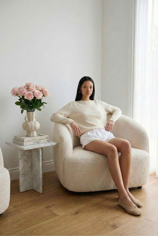 Model wearing Shea Skort in White Cotton-Blend Poplin Mini Skort with Drawstring paired with knit sweater and flats posing in feminine minimalist living room