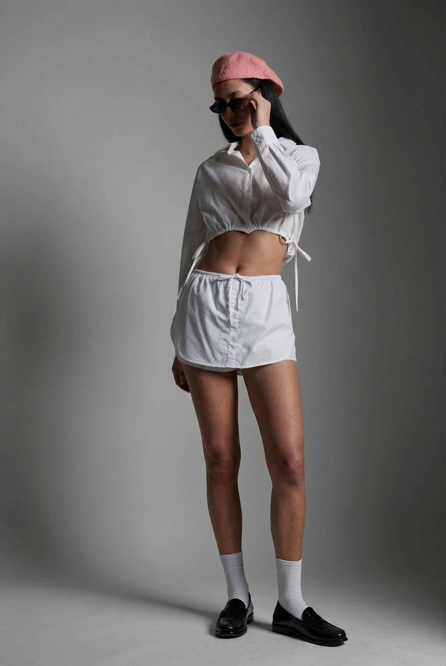 Model wearing Shea Skort in White Cotton-Blend Poplin Mini Skort with Drawstring paired with matching crop top and shiny loafers with tall socks
