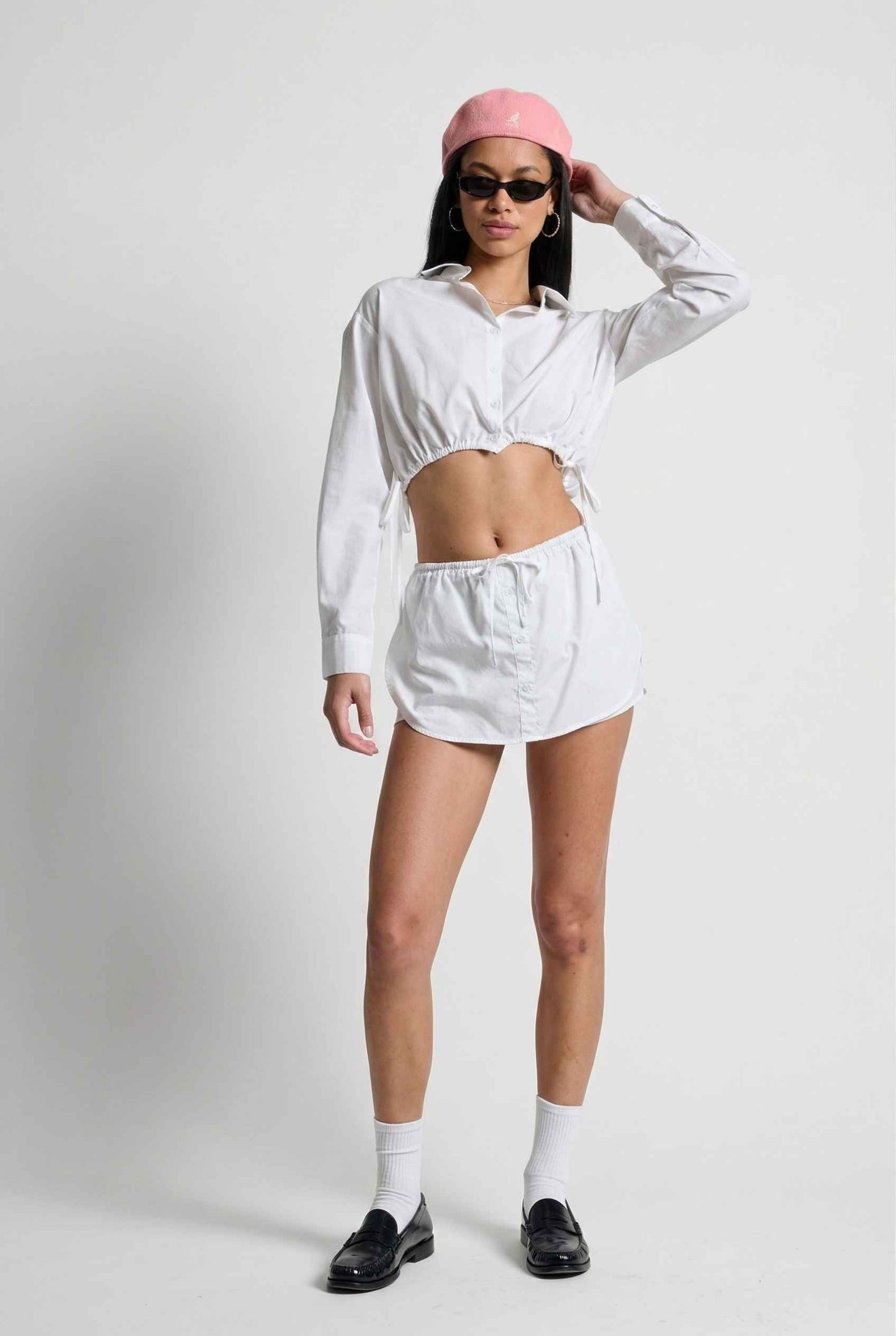 Model wearing Shea Skort in White Cotton-Blend Poplin Mini Skort with Drawstring paired with matching crop top and shiny loafers with tall socks