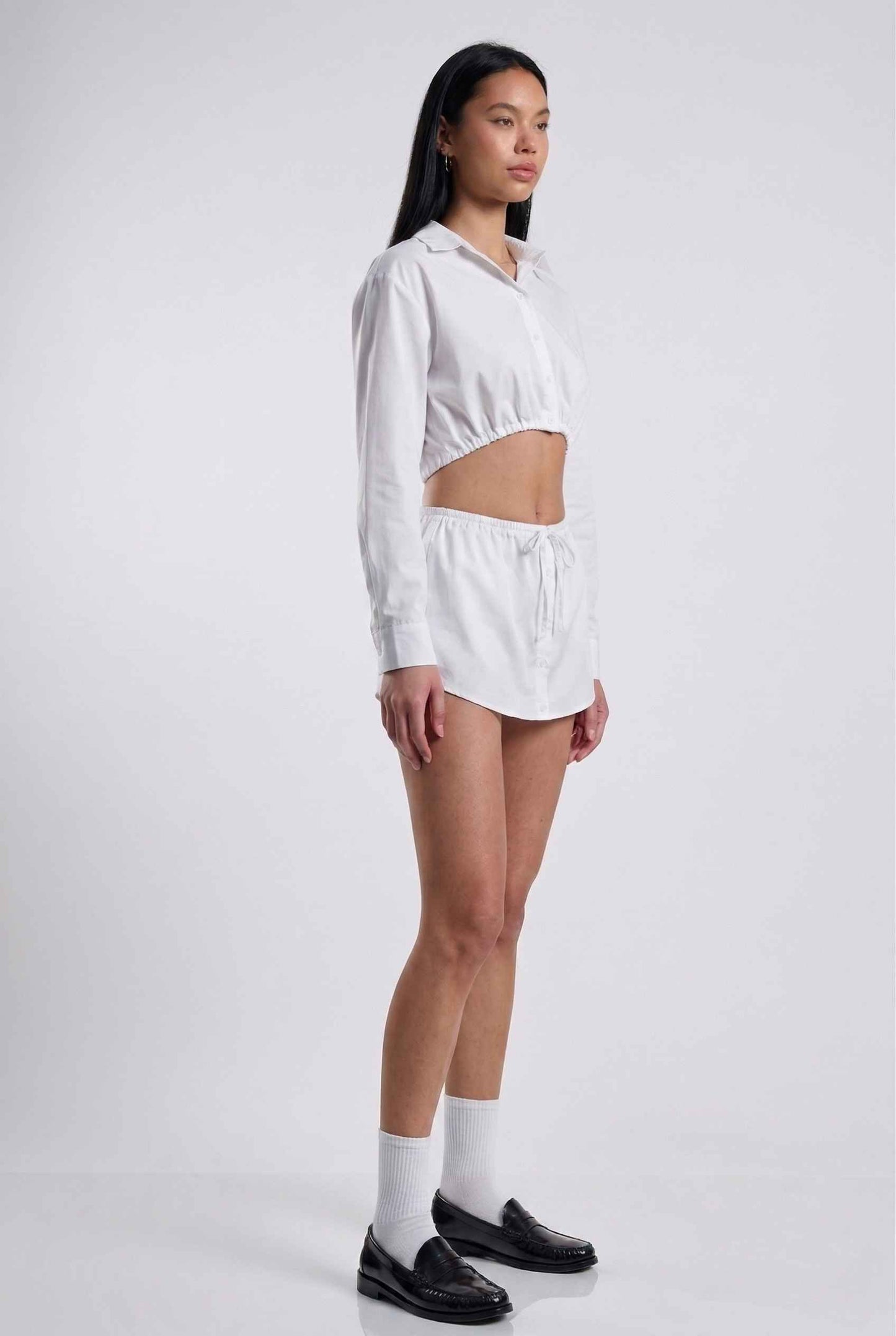 Model wearing Shea Skort in White Cotton-Blend Poplin Mini Skort with Drawstring paired with matching crop top and shiny loafers with tall socks