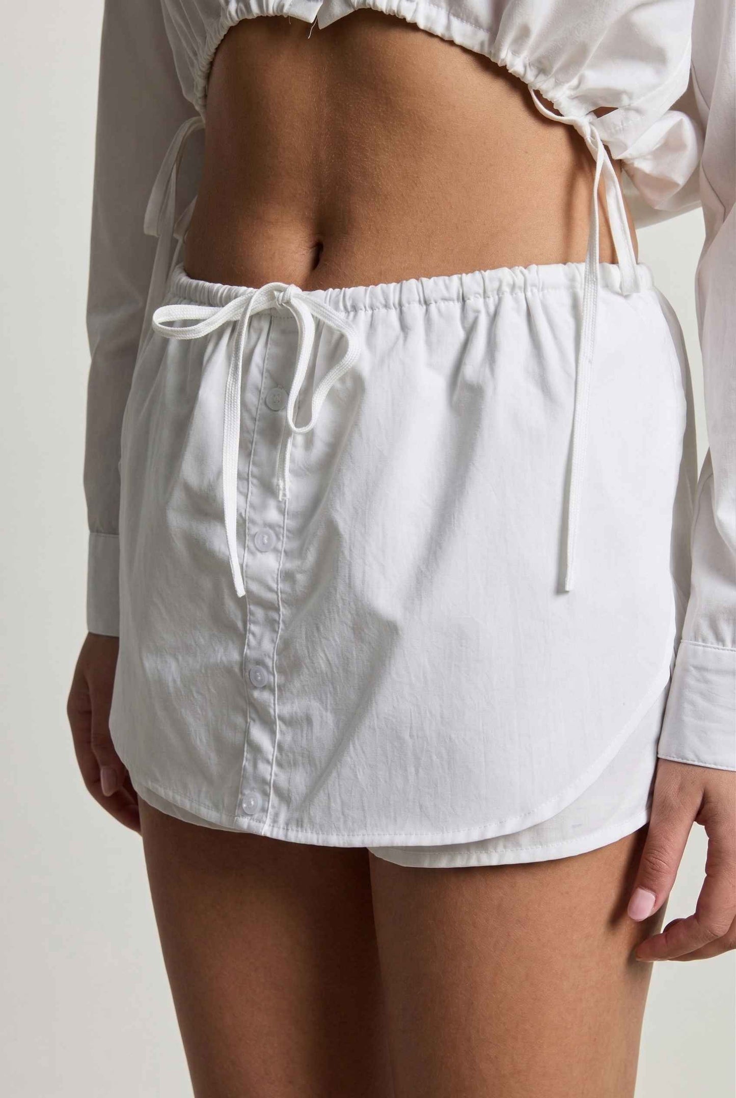 Model wearing Shea Skort in White Cotton-Blend Poplin Mini Skort with Drawstring paired with matching crop top close up cotton detail tied