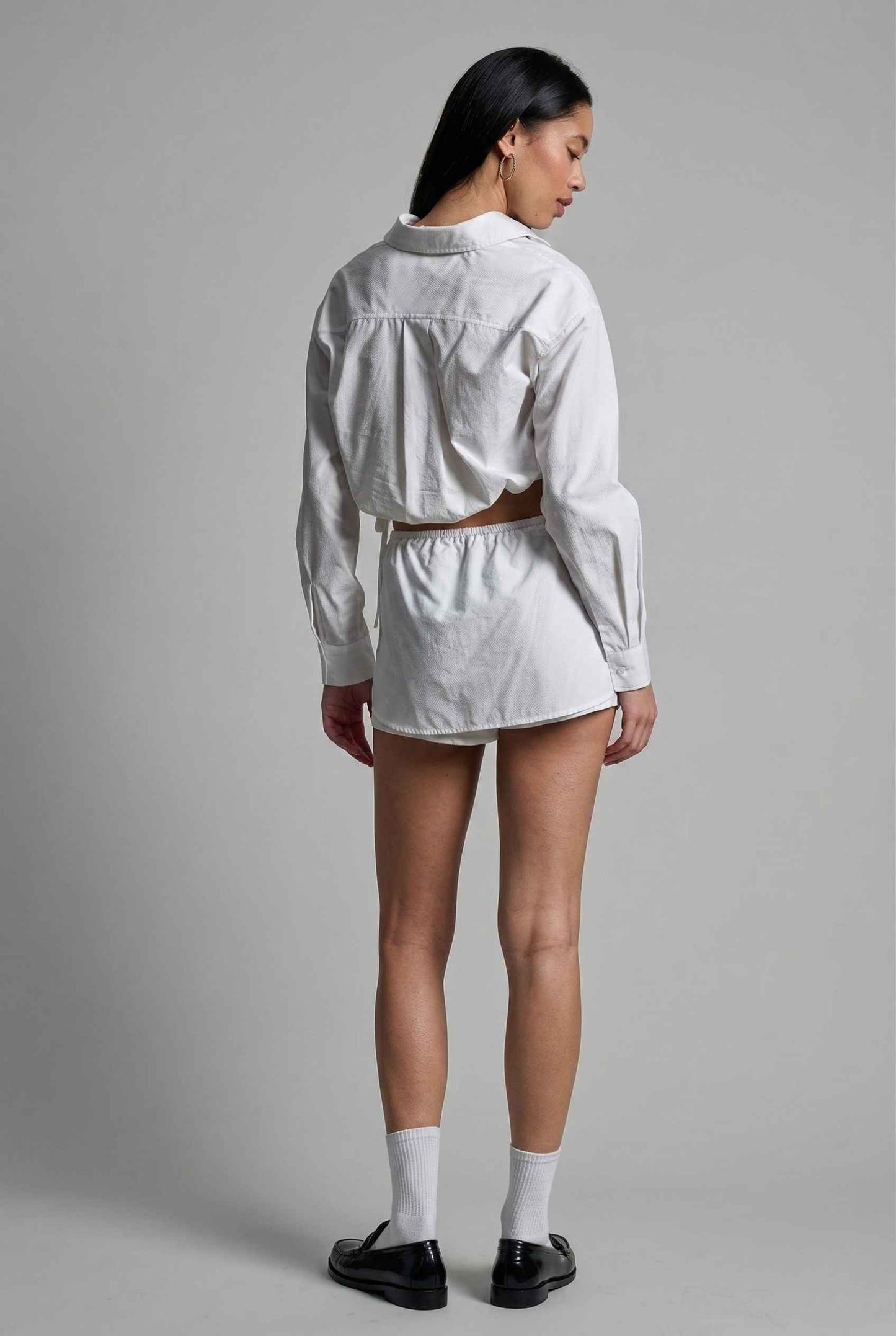 Model wearing Shea Skort in White Cotton-Blend Poplin Mini Skort with Drawstring paired with matching crop top and shiny loafers with tall socks