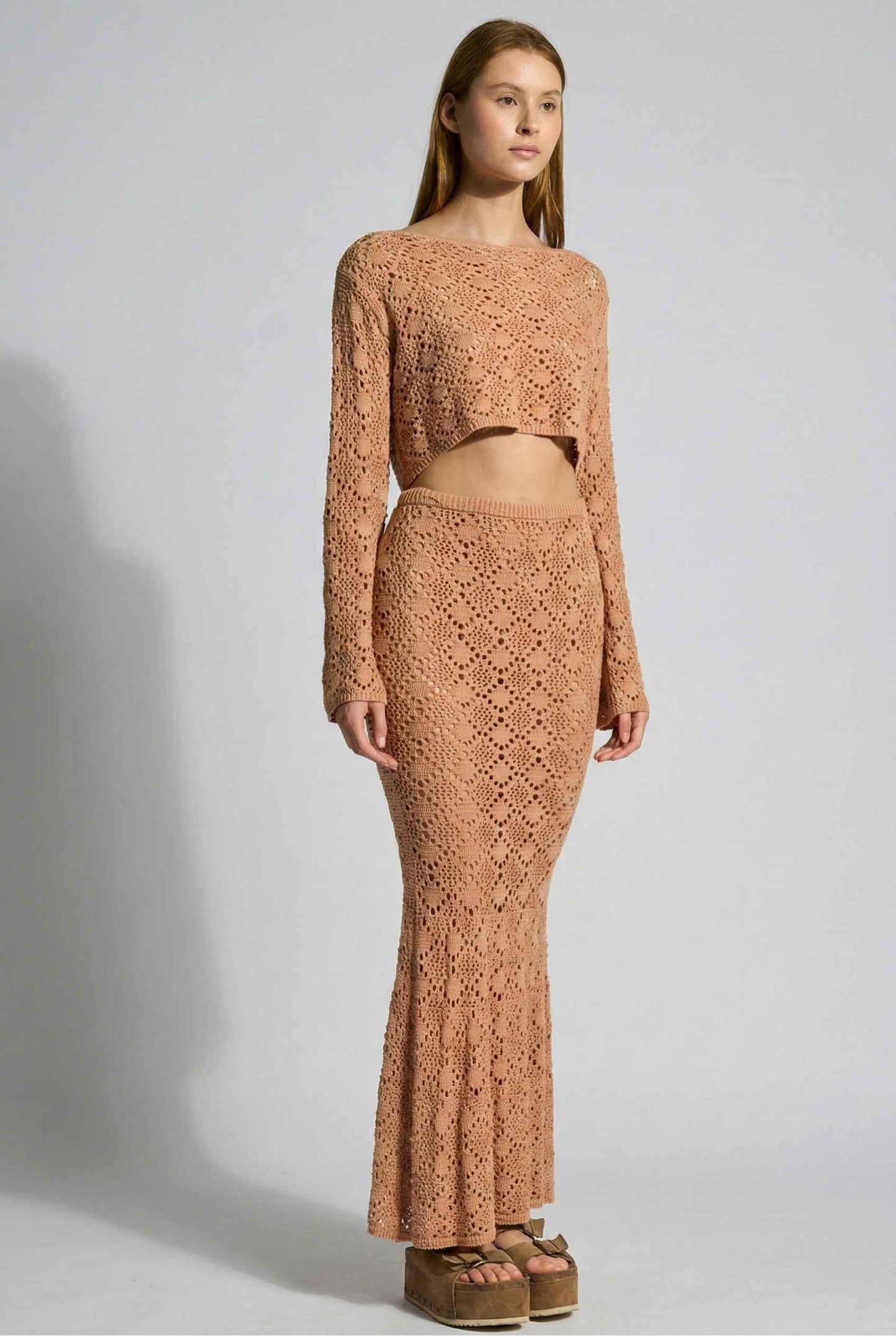 Model wearing Siren Skirt Open-Knit Crochet Mermaid Maxi Skirt in Camel Tan with matching crop top and platform sandals on plain background