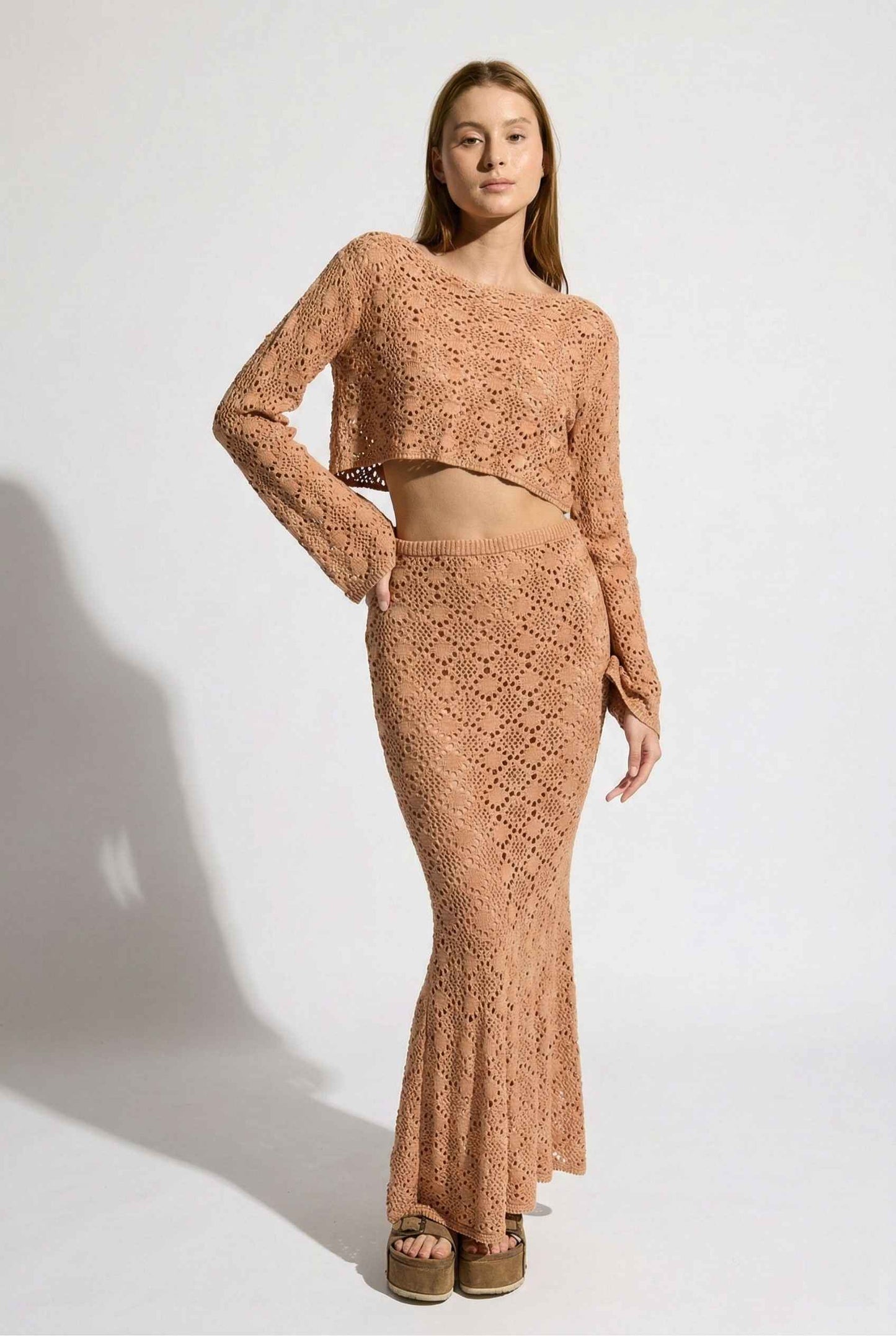 Model wearing Siren Skirt Open-Knit Crochet Mermaid Maxi Skirt in Camel Tan with matching crop top and platform sandals on plain background