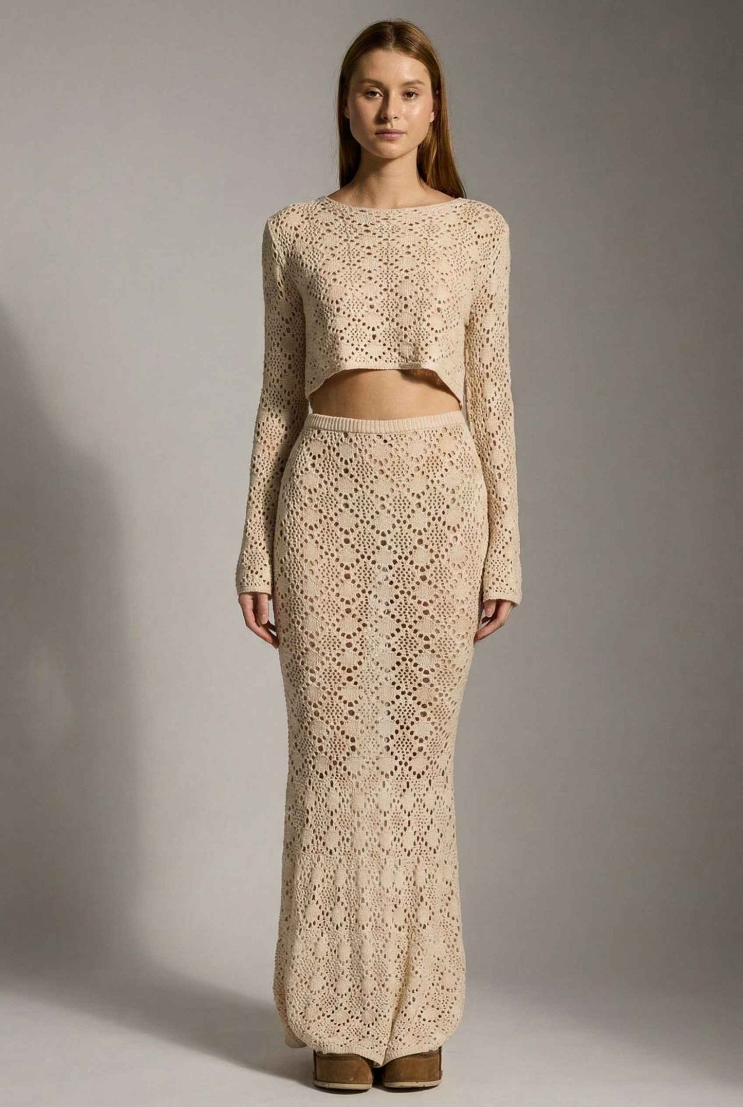 Model wearing Siren Skirt Open-Knit Crochet Mermaid Maxi Skirt in Sand Cream with matching crop top and platform sandals on plain background