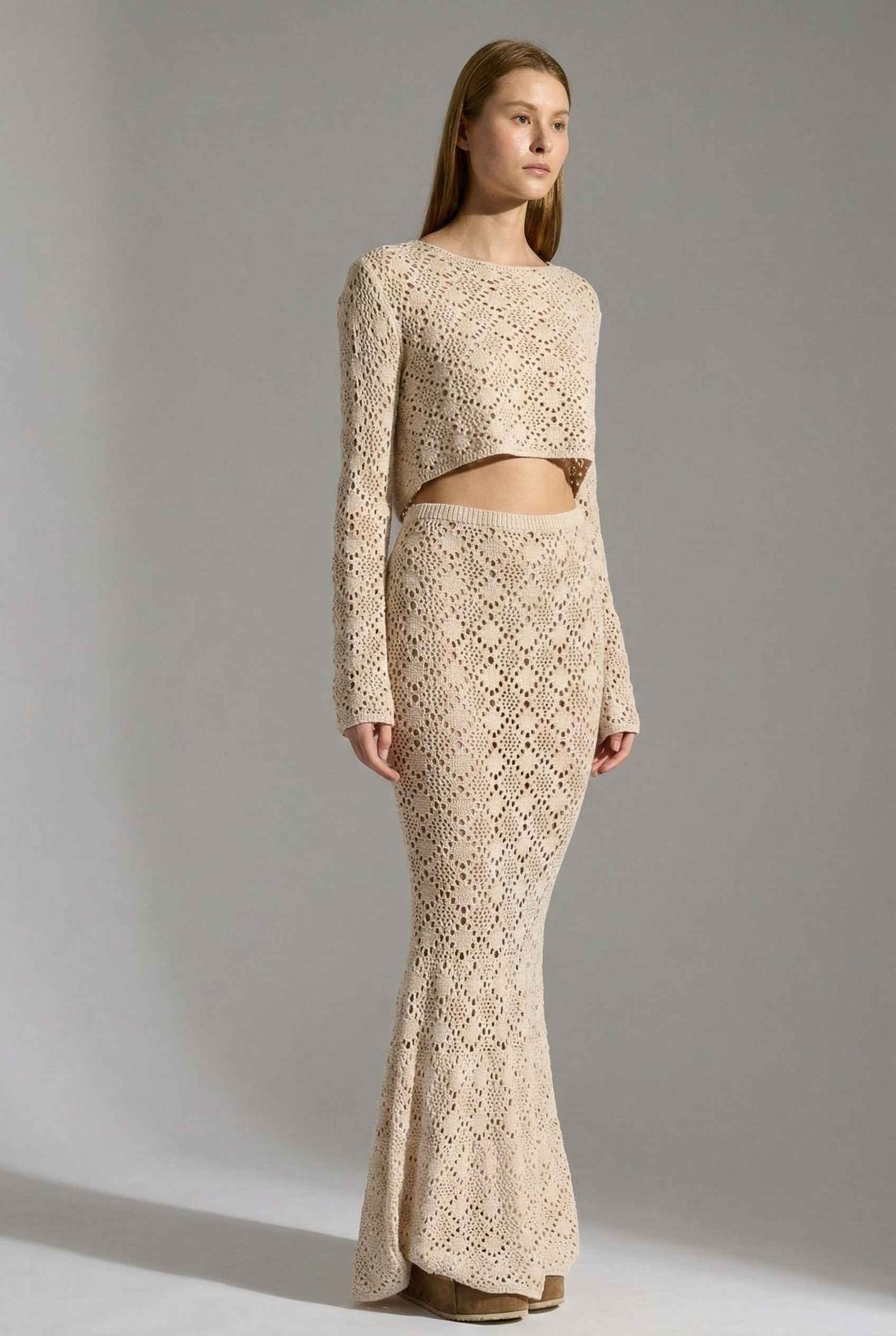 Model wearing Siren Skirt Open-Knit Crochet Mermaid Maxi Skirt in Sand Cream with matching crop top and platform sandals on plain background