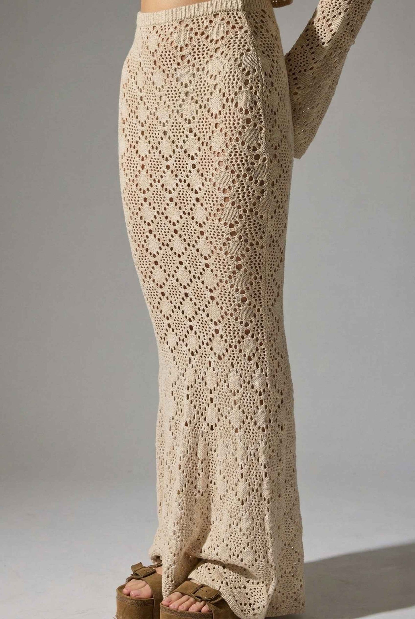 Model wearing Siren Skirt Open-Knit Crochet Mermaid Maxi Skirt in Sand Cream with matching crop top and platform sandals on plain background