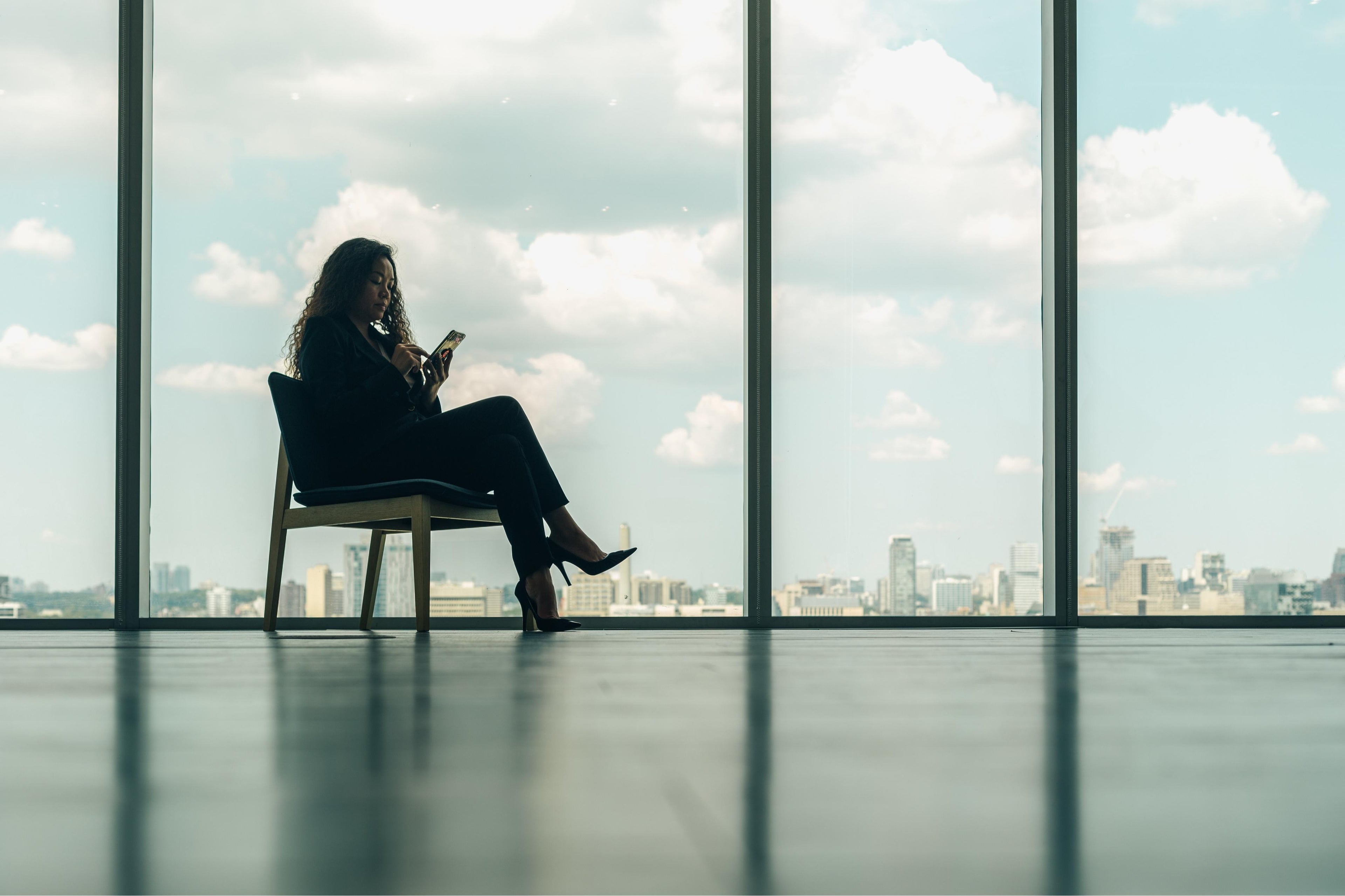 Woman sitting on a chair by large windows with a cityscape view
