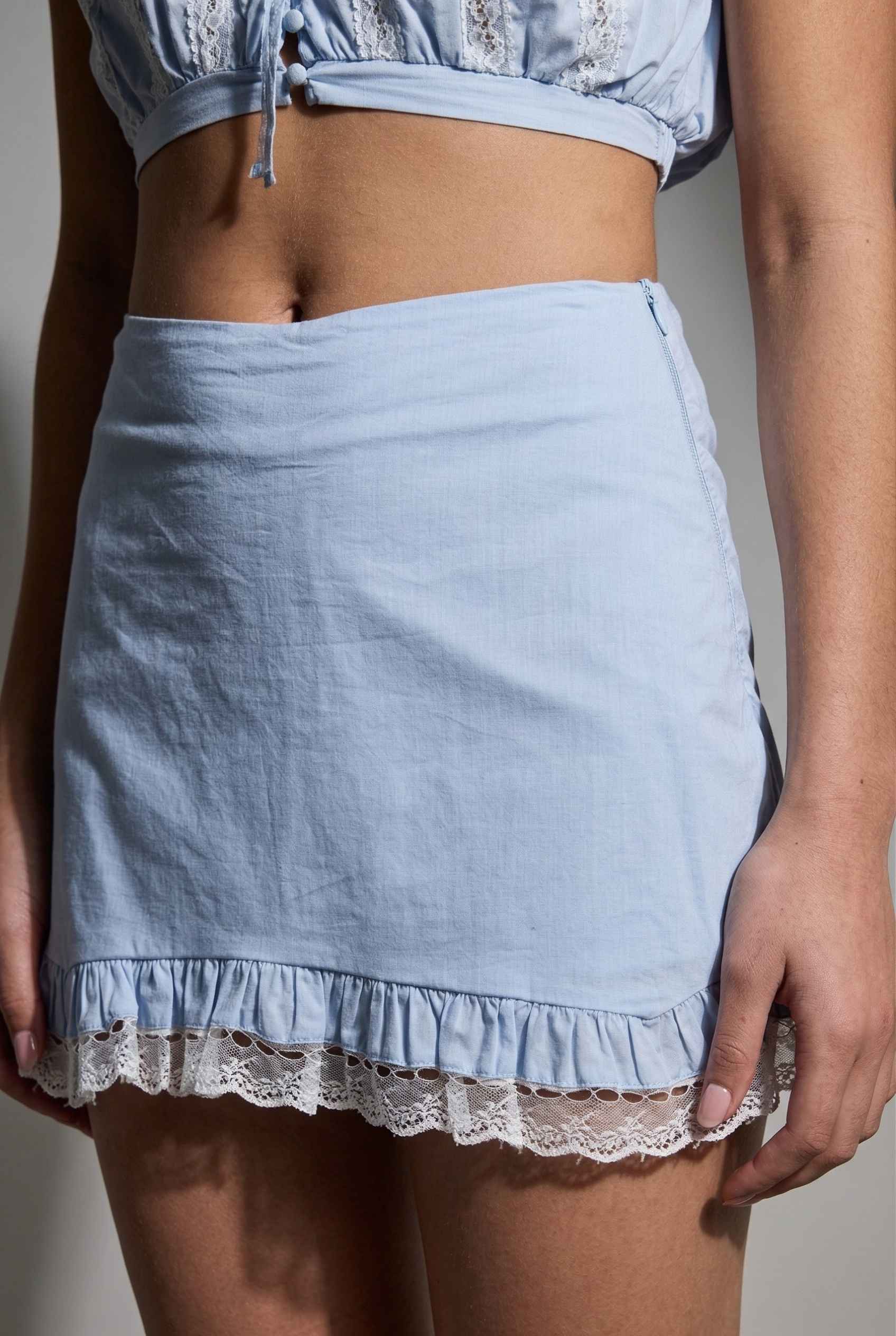 Model wearing Skye Skirt in Light Blue Cotton Mini Skirt with Delicate Lace Trim paired with matching top close up lace detail