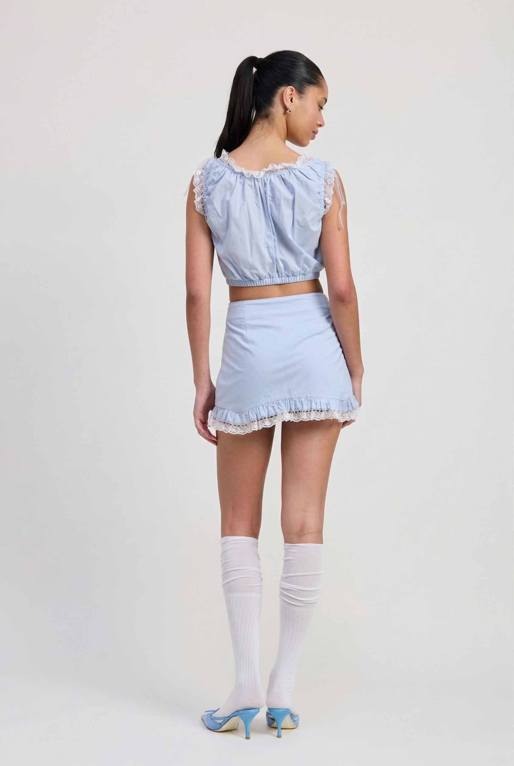 Model wearing Skye Skirt in Light Blue Cotton Mini Skirt with Delicate Lace Trim paired with matching top and heels with knee stockings