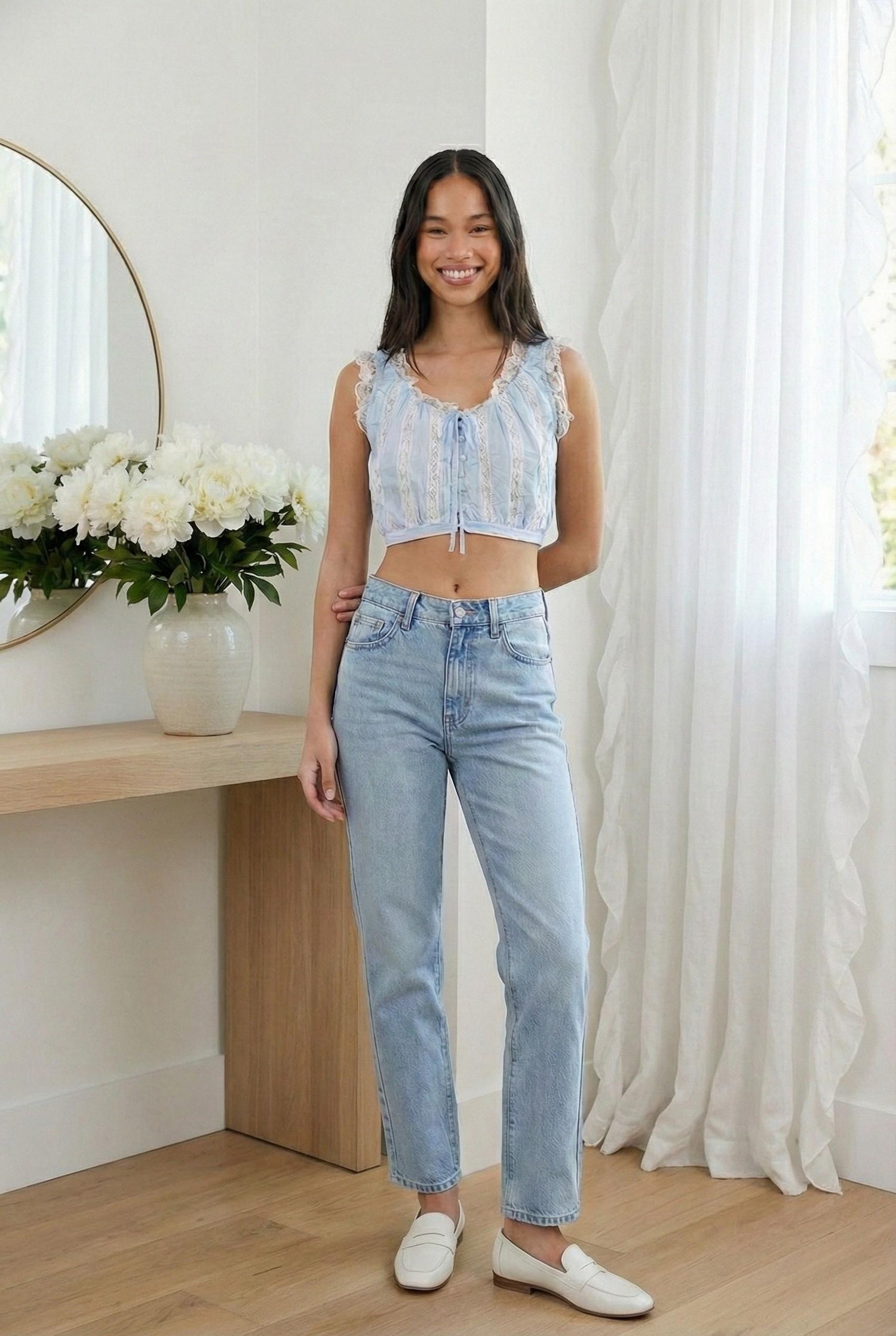 Model wearing Emory Park sleeveless lace ruffled top in Light Blue styled with jeans and loafers posing in minimalist feminine home