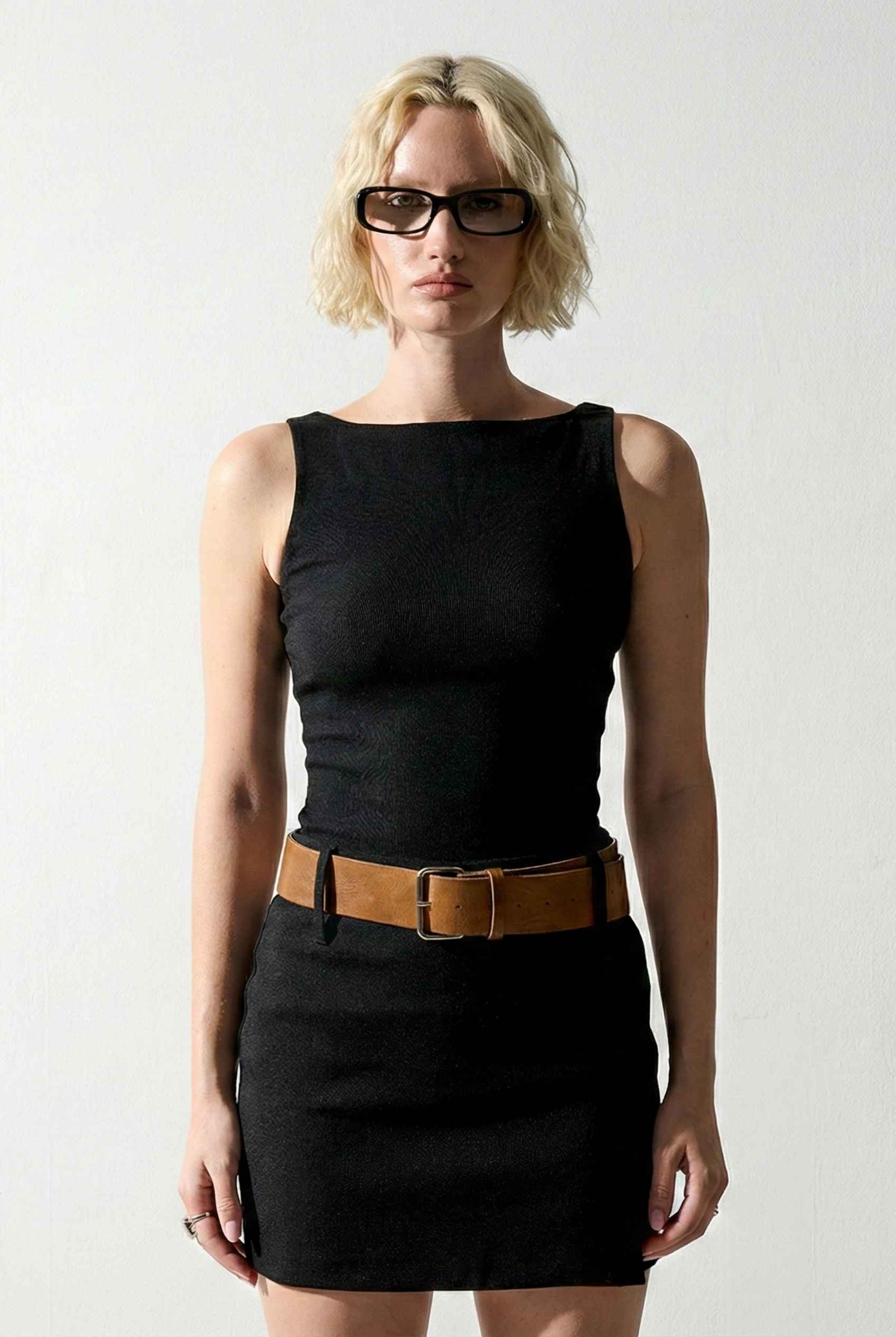 Woman wearing a Sloane Mini Black Boat Neck Structured Knit Dress with a brown belt against a white background