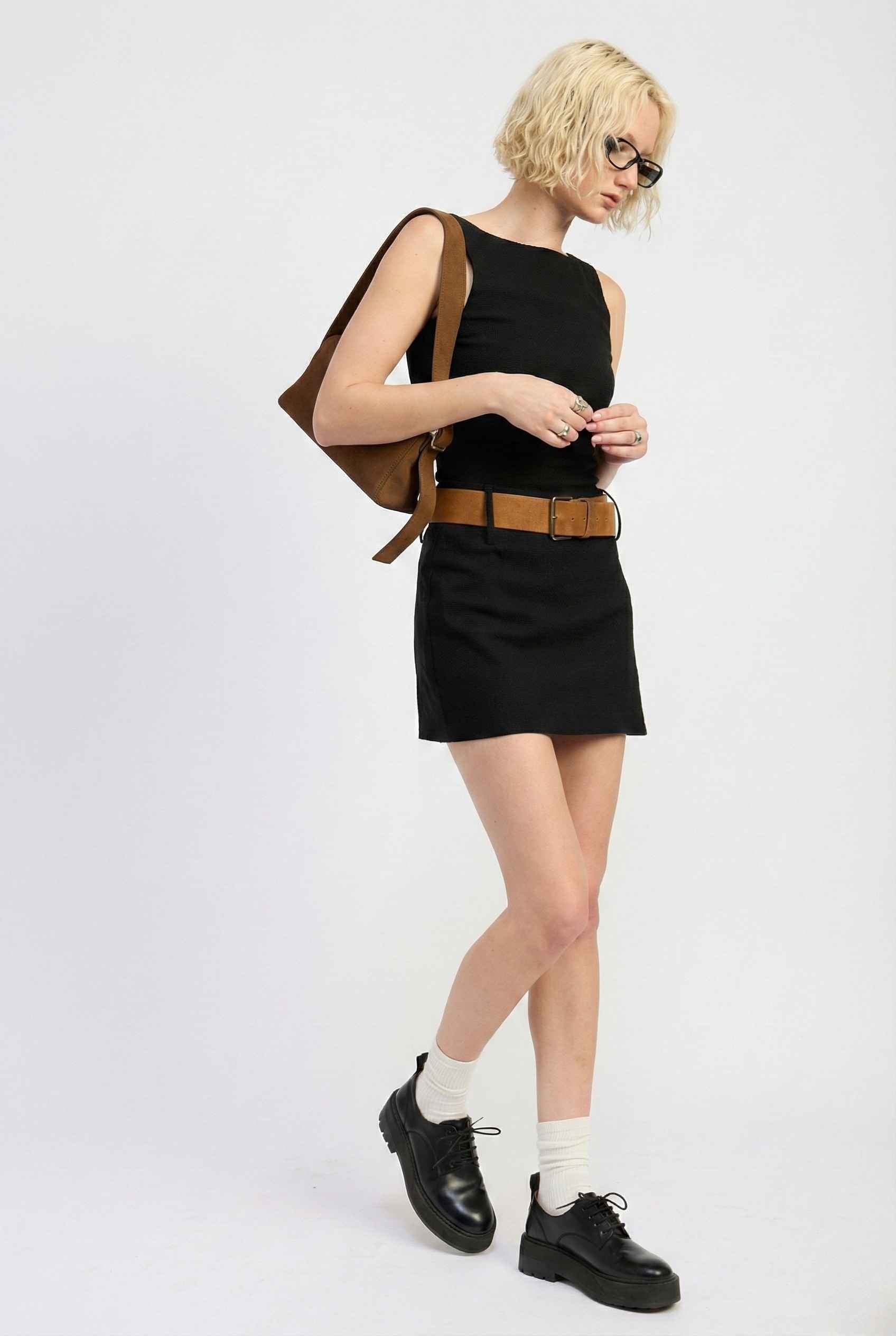 Woman wearing a Sloane Mini Black Boat Neck Structured Knit Dress with a brown backpack on a white background