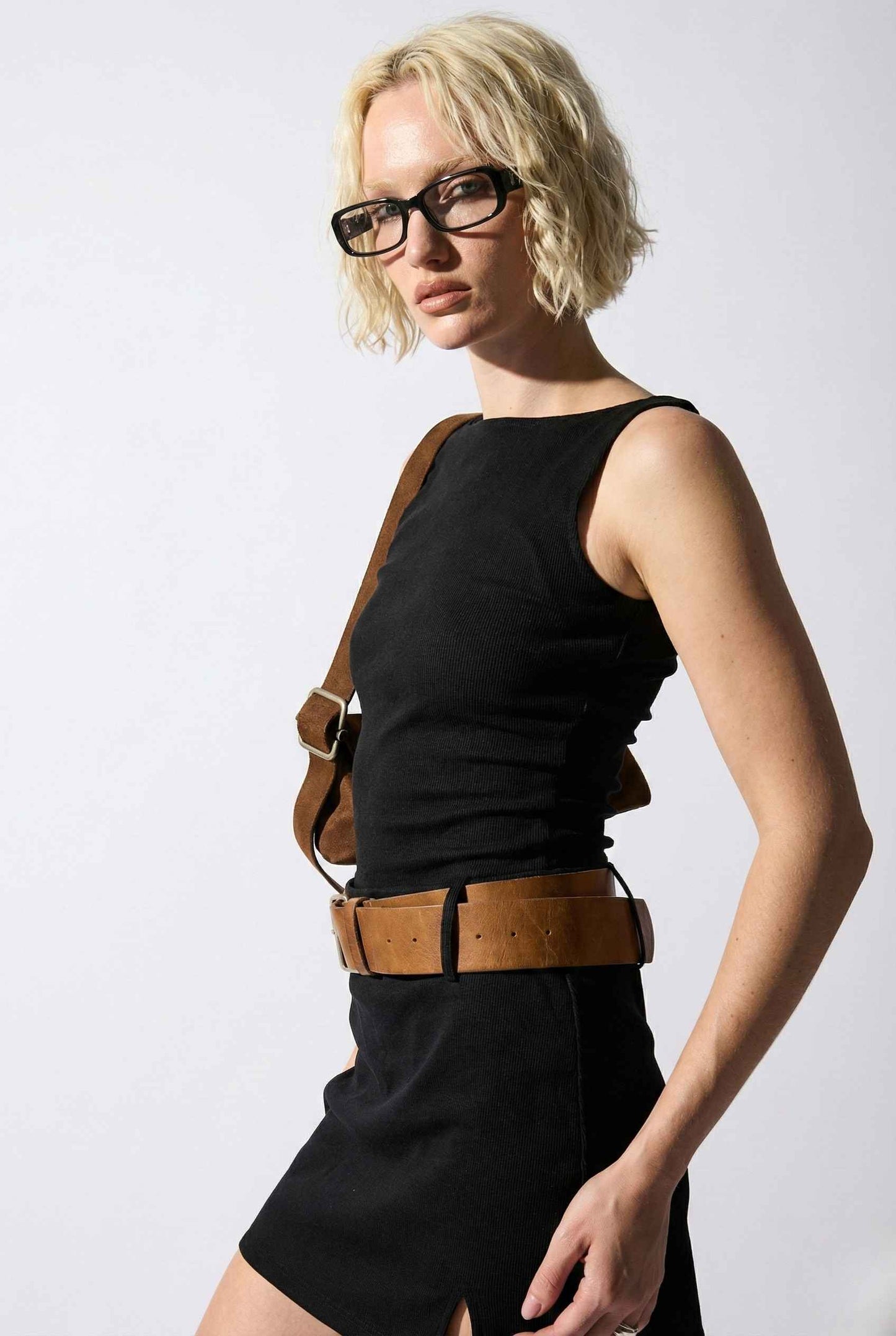Woman wearing a Sloane Mini Black Boat Neck Structured Knit Dress with a brown belt and shoulder bag on a white background