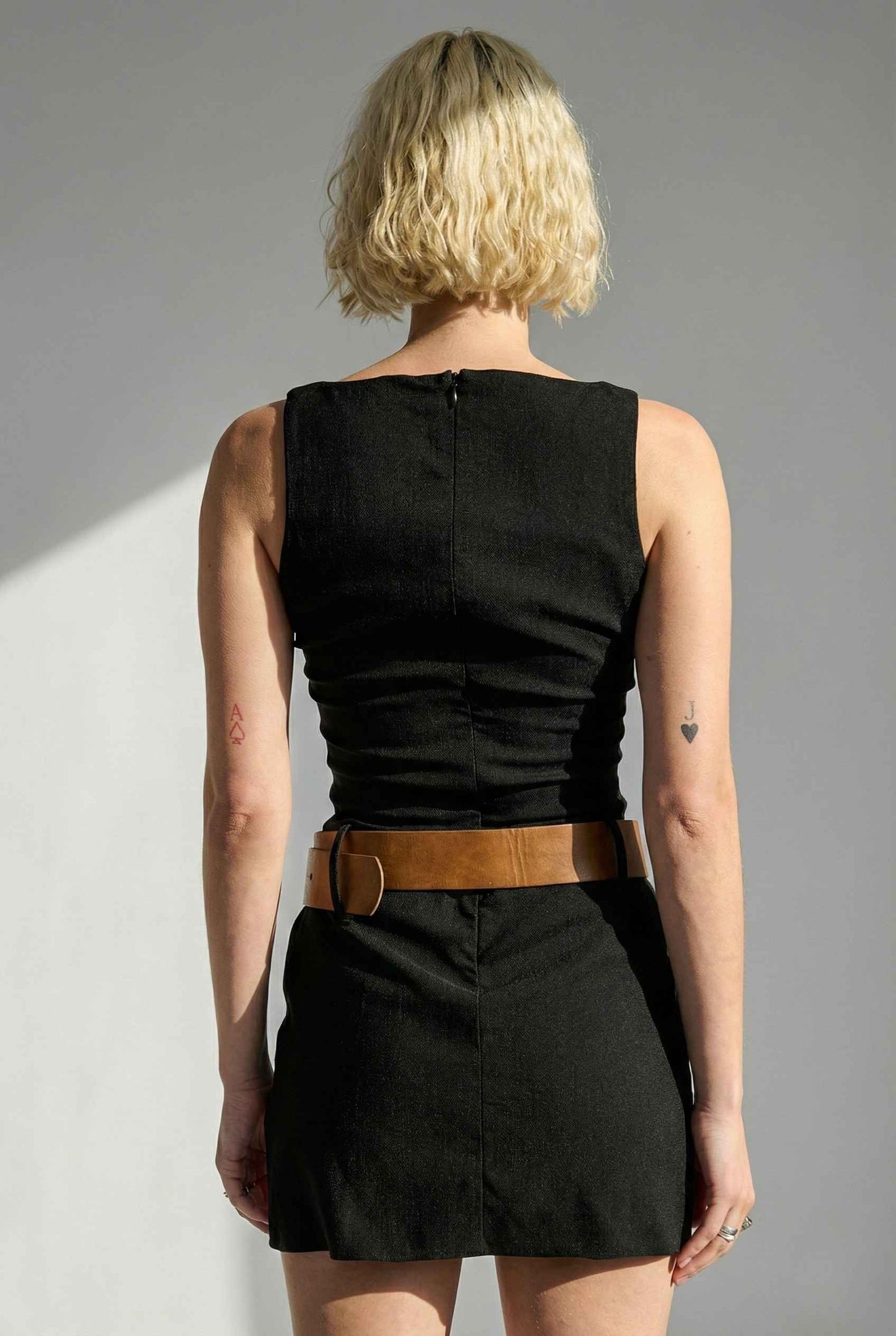 Person wearing a Sloane Mini Black Boat Neck Structured Knit Dress with a brown belt against a gray background
