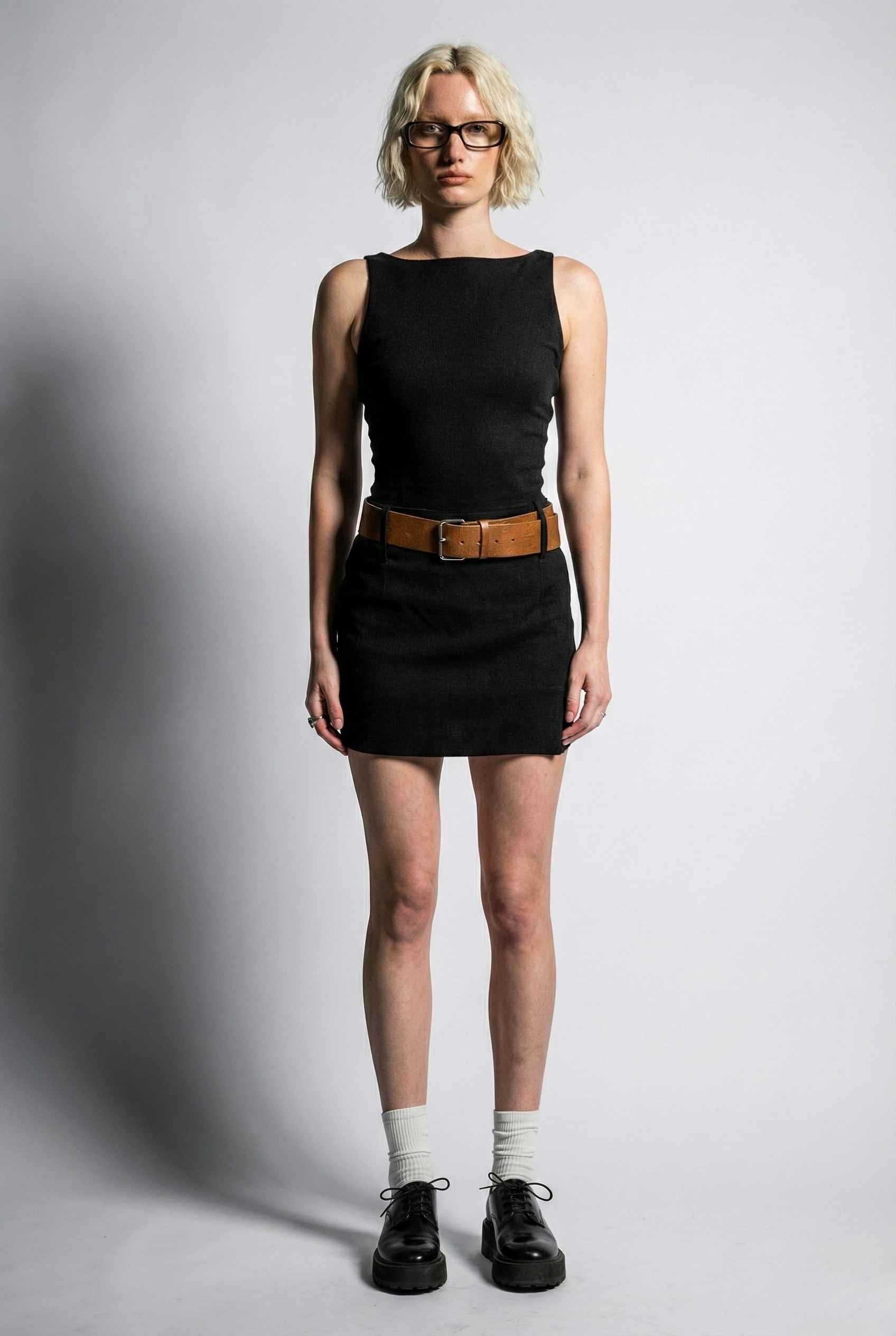 Person wearing a Sloane Mini Black Boat Neck Structured Knit Dress with a brown belt on a plain background