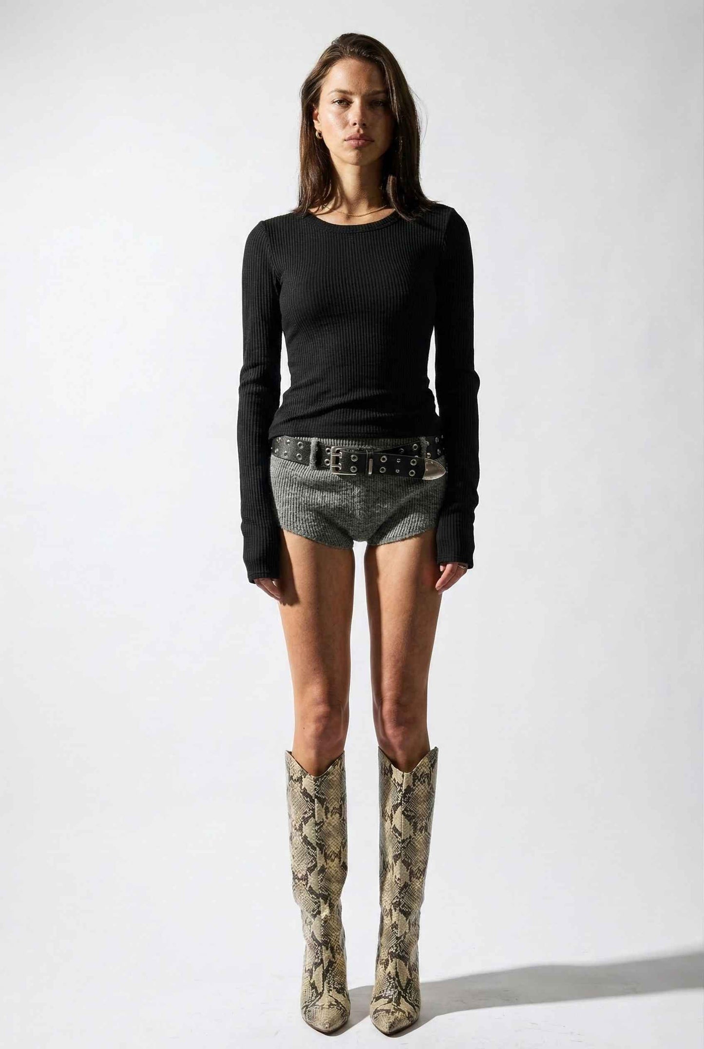 Model wearing Sloane Top in Black Cotton-Rayon Ribbed Crew Neck Long Sleeve Tee with knit shorts, belt, and tall snake boots