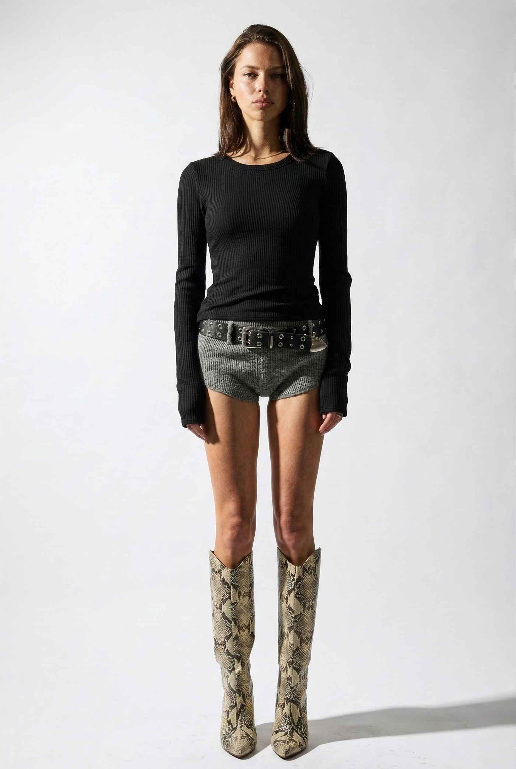 Model wearing Sloane Top in Black Cotton-Rayon Ribbed Crew Neck Long Sleeve Tee with knit shorts, belt, and tall snake boots