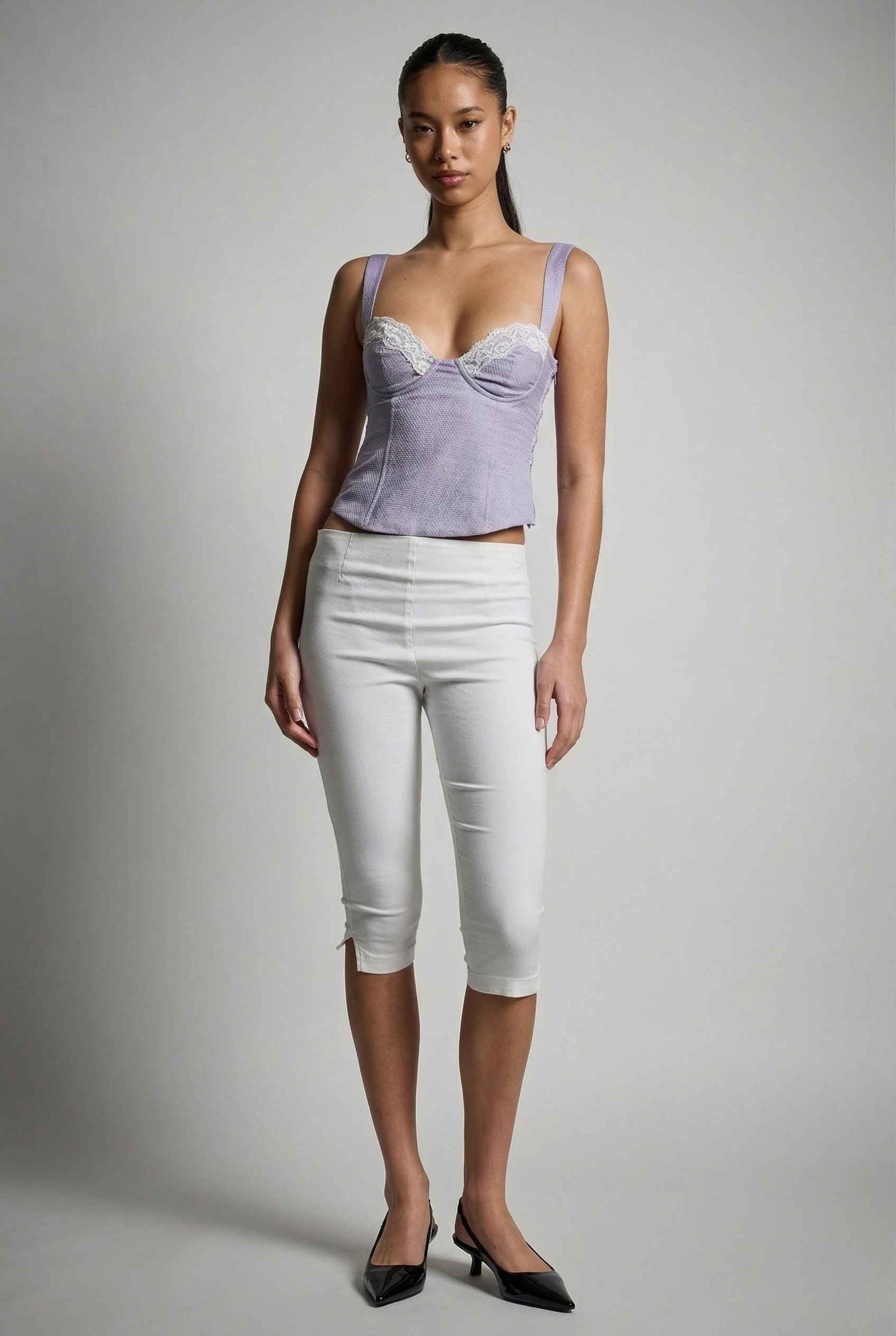Woman wearing a Sophie Top Blue Pastel Satin Corset Cami with White Lace Trim and white pants against a plain background