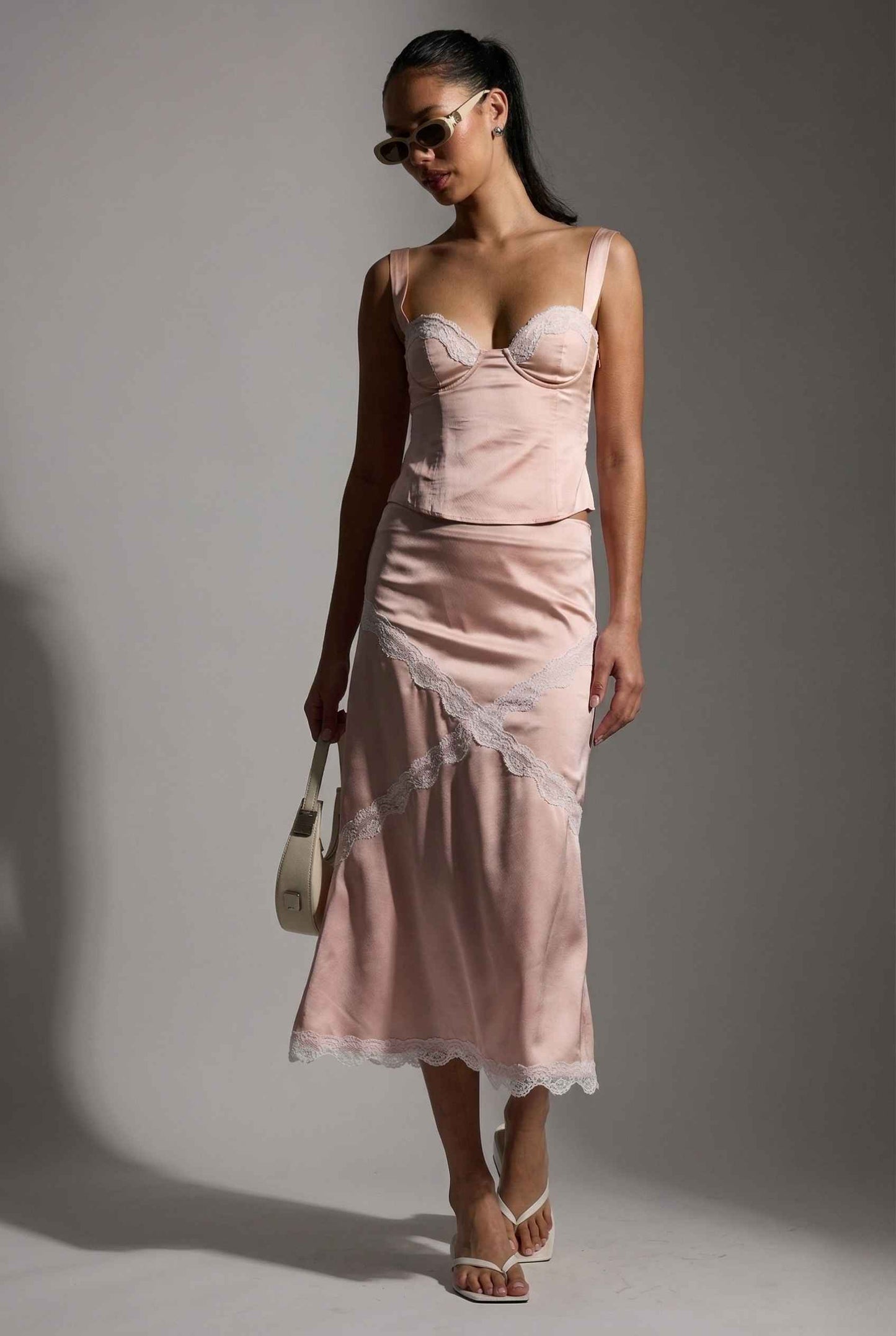 Woman wearing a Sophie Top Pink Pastel Satin Corset Cami with White Lace Trim with lace details against a gray background