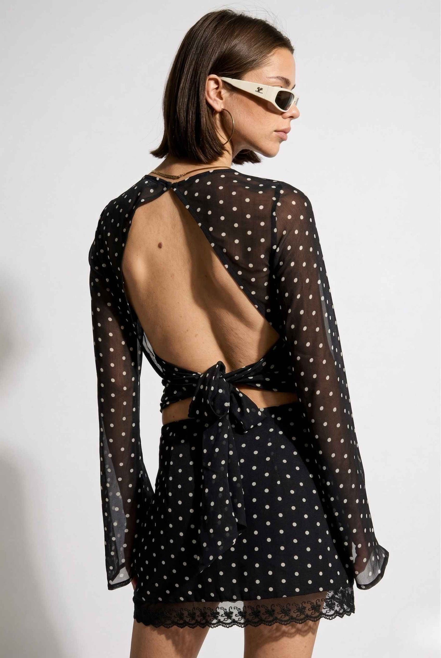 Woman wearing a Stella Top Black & White Polka Dot Sheer Long Sleeve with sheer sleeves and open back on a white background