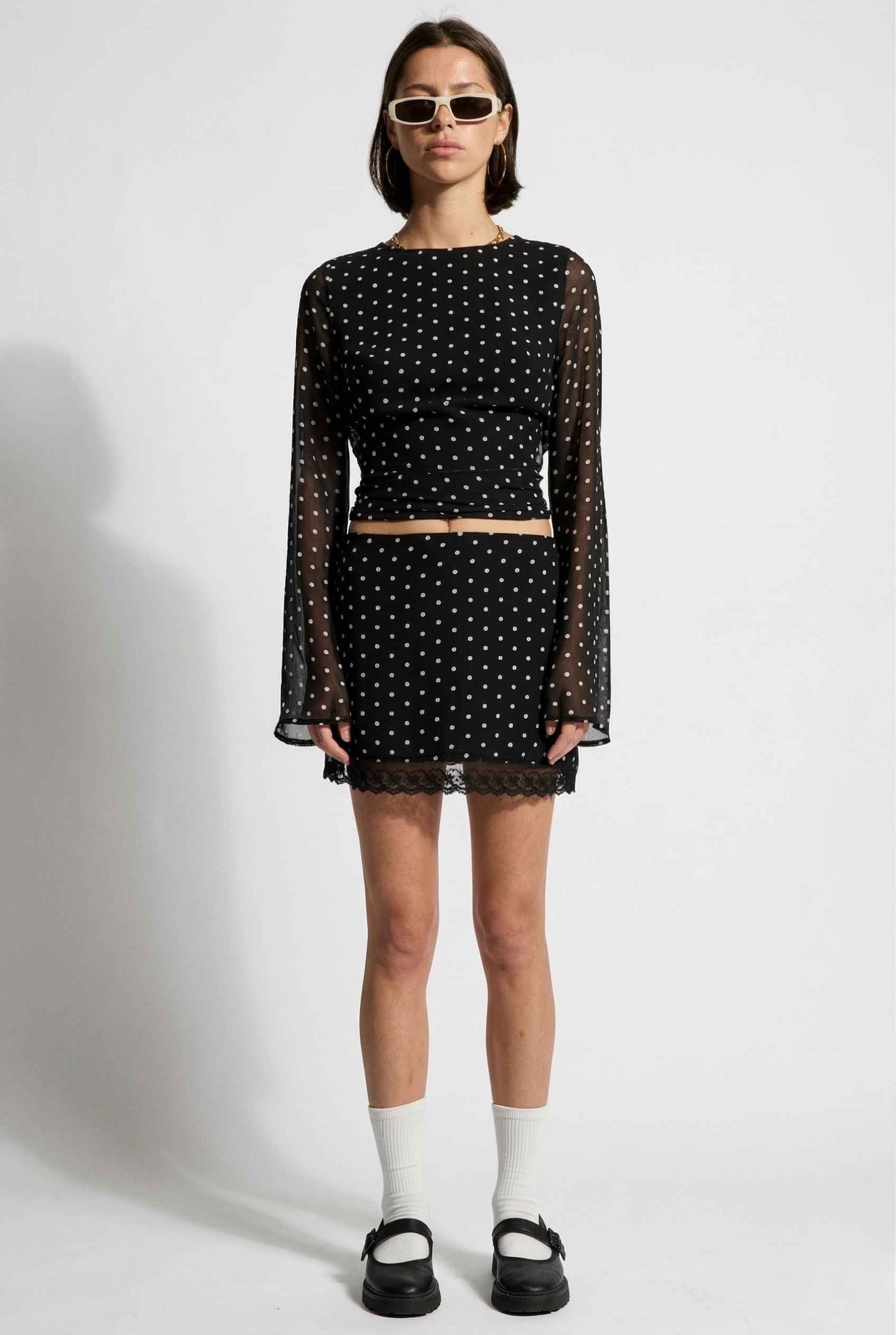 Woman wearing a Stella Top Black & White Polka Dot Sheer Long Sleeve with sheer sleeves on a white background