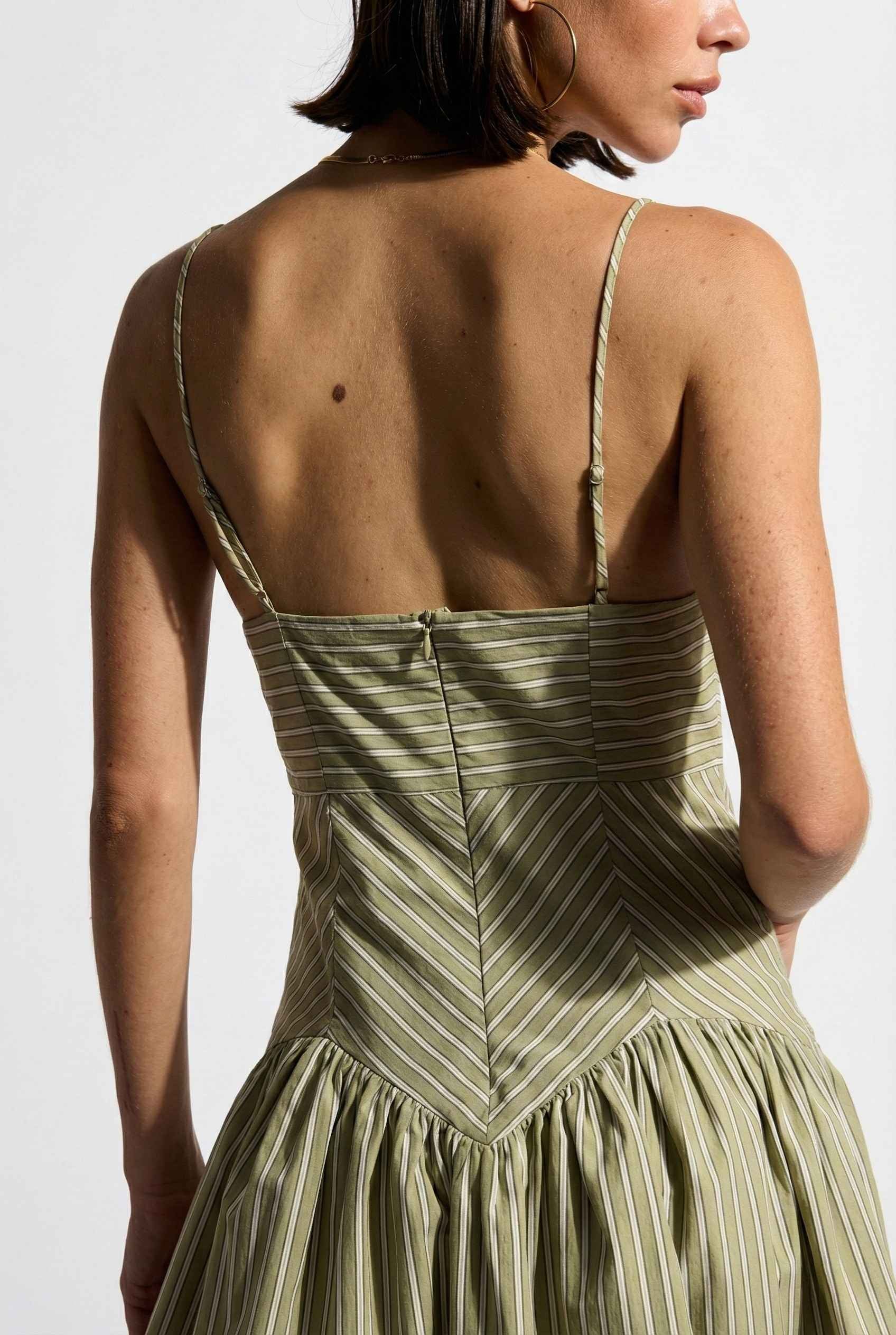 Woman wearing a Sutton Mini Sage Stripe Drop Waist Cotton Dress with thin straps on a white background
