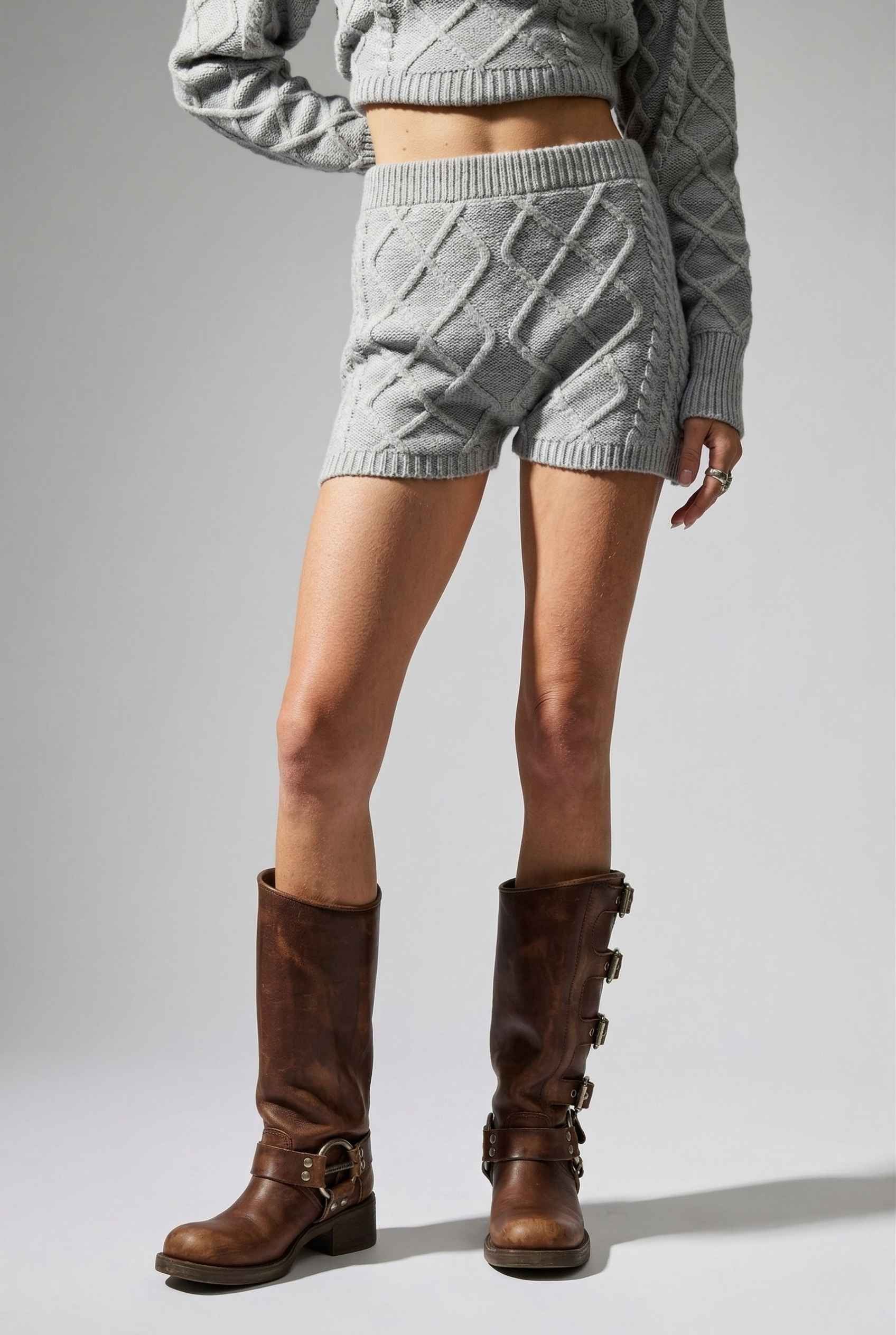 Model wearing Sutton Shorts in Grey Cable Knit High-Waist Lounge Shorts paired with matching crop sweater and knee-high riding boots