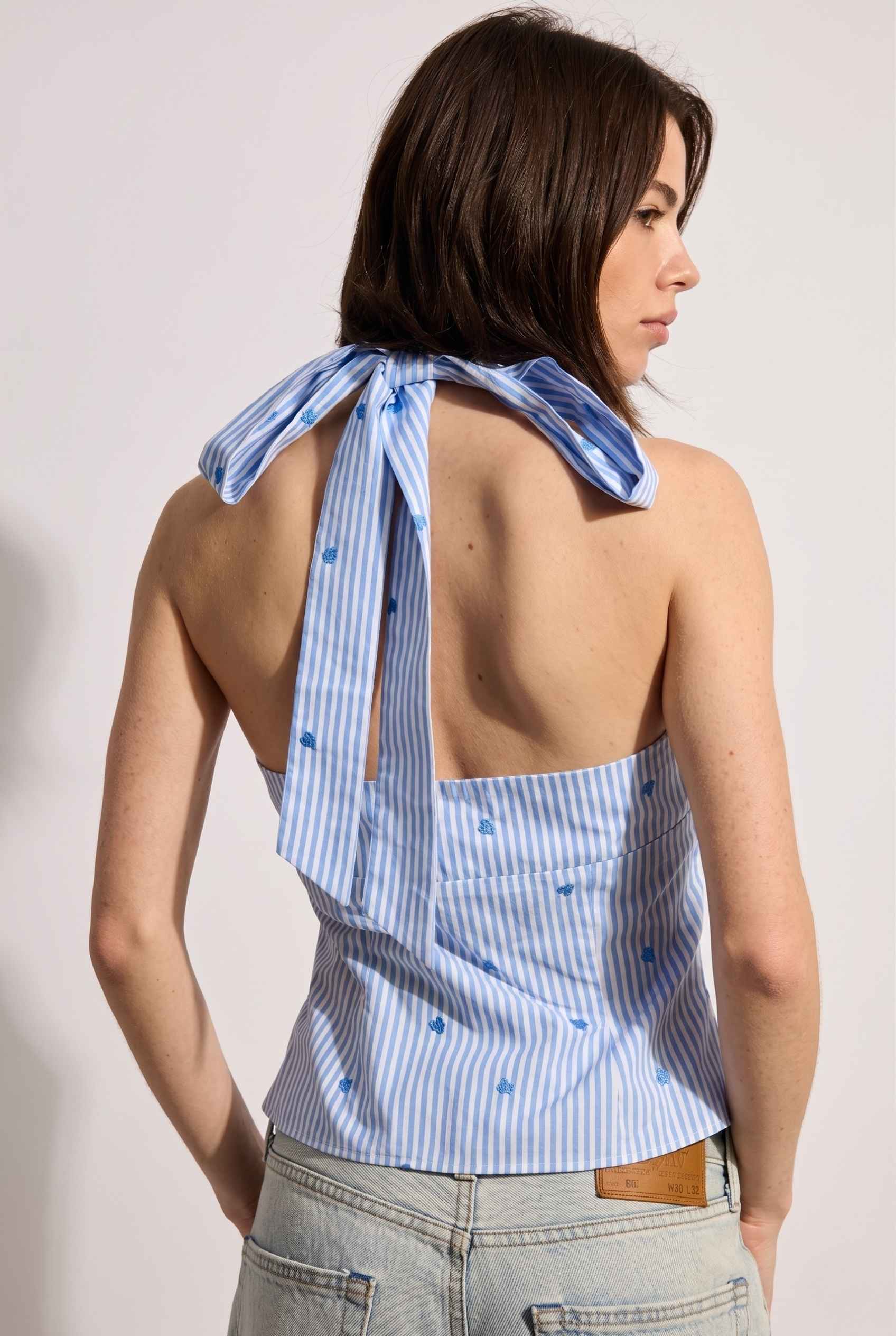 Model wearing Sara Cross-Neck Striped Cotton Halter Top Heart Embroidered Tank Top in Blue with jeans tie-up back detail