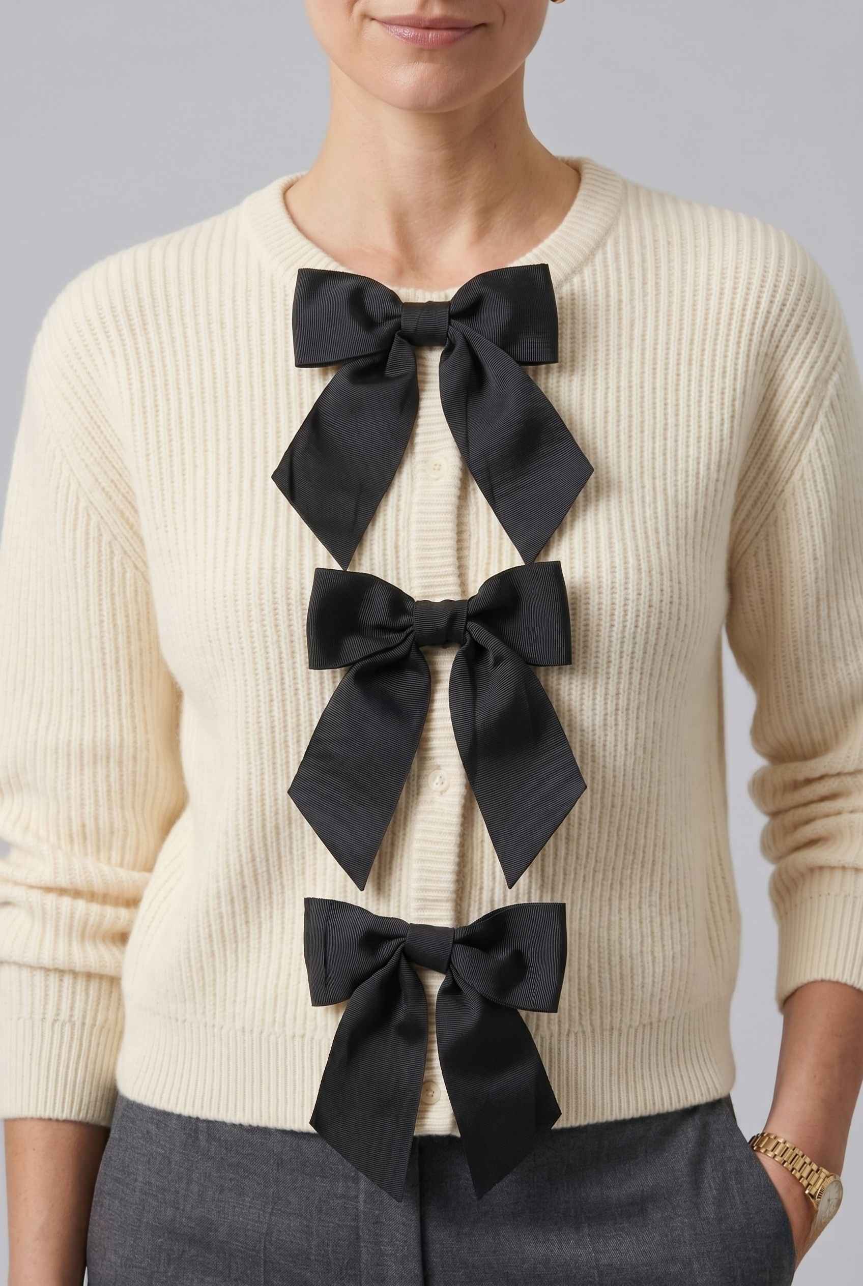 The Camille Bow Cardigan Ribbed Shaker Cream Knit Sweater worn by a woman on a gray background