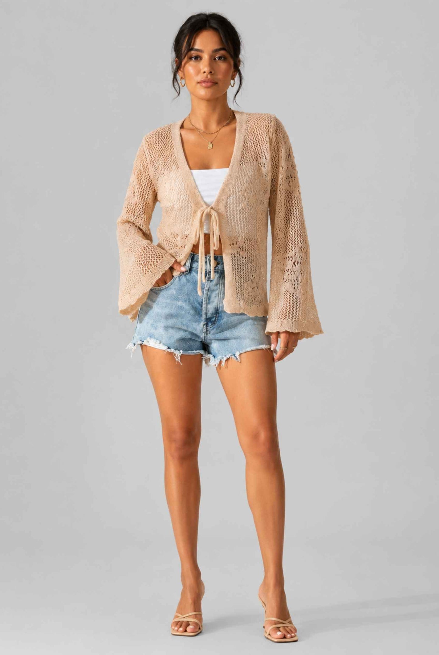 Woman wearing The Faye Tie-Front Cardigan Open Stitch Beige Crochet Cardigan on a gray background