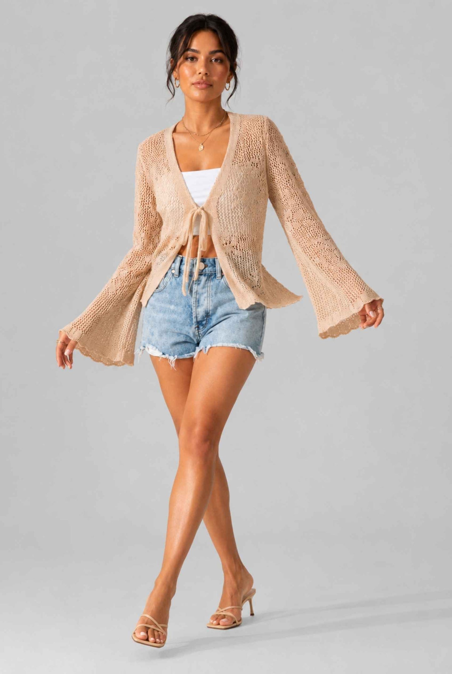Woman wearing The Faye Tie-Front Cardigan Open Stitch Beige Crochet Cardigan on a gray background