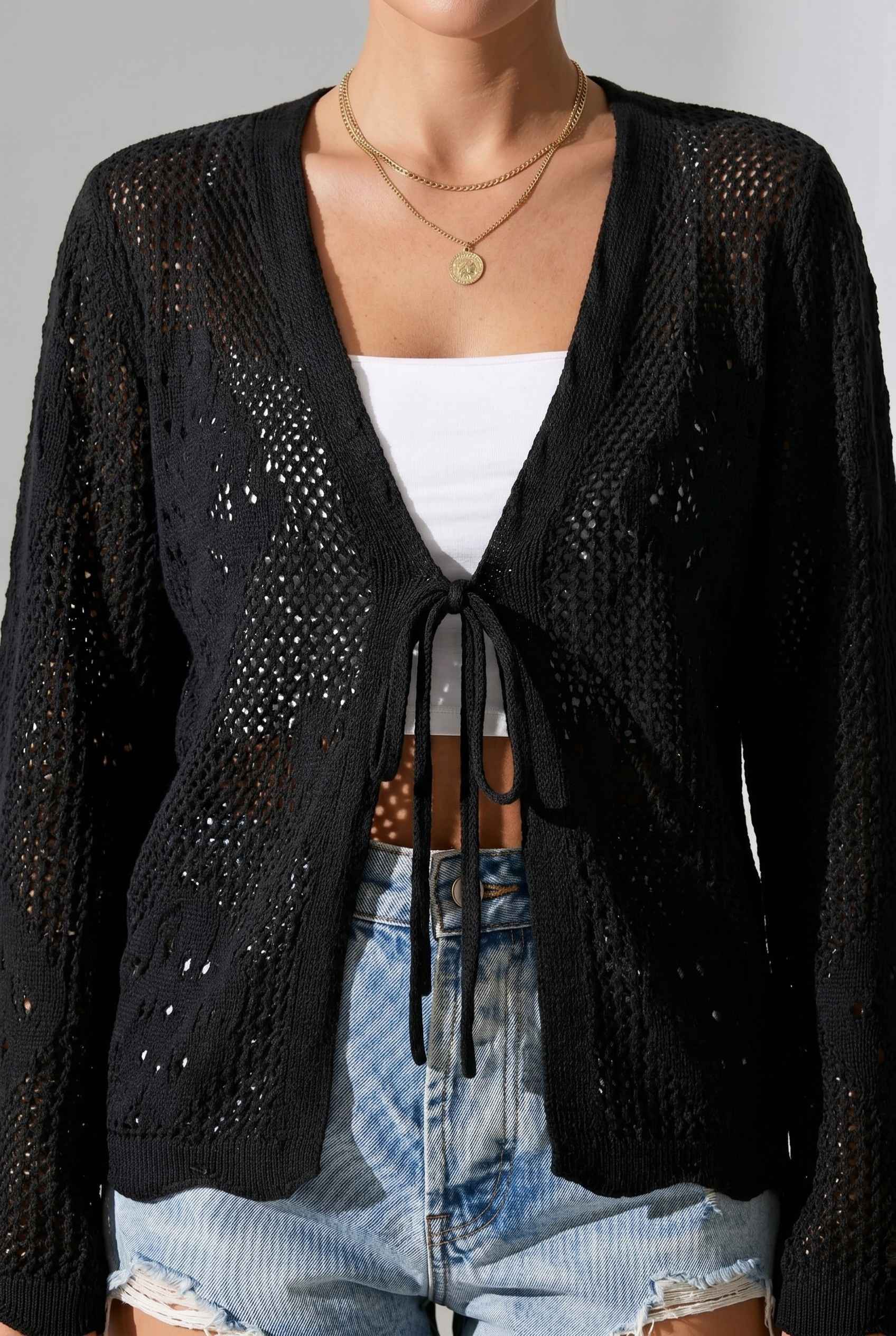 Woman wearing The Faye Tie-Front Cardigan Open Stitch Black Crochet Cardigan over a top and blue jeans.