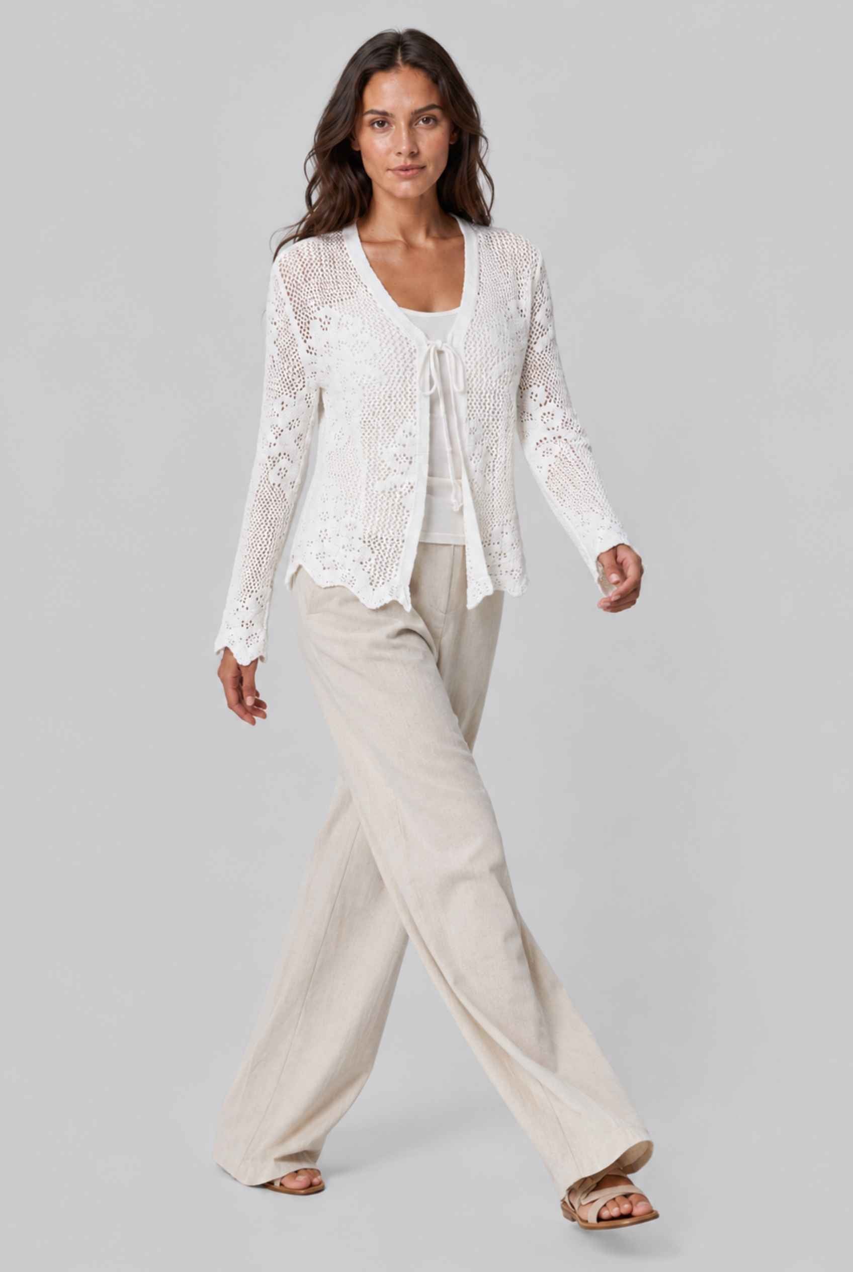 Woman wearing aThe Faye Tie-Front Cardigan Open Stitch White Crochet Cardigan on a gray background