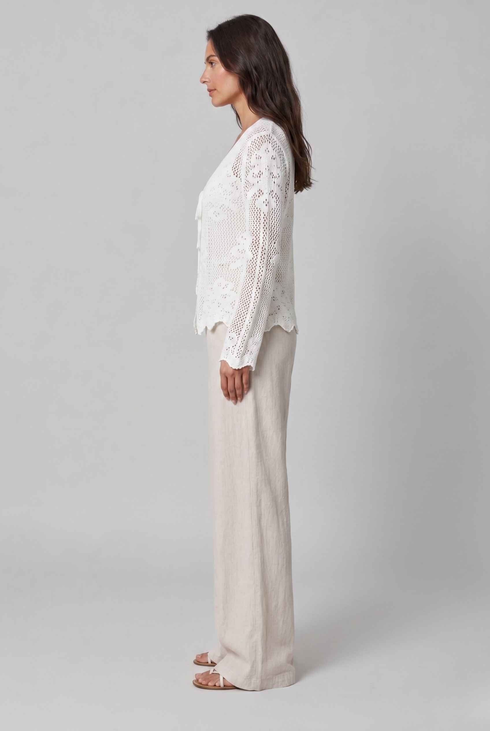 Woman wearing The Faye Tie-Front Cardigan Open Stitch White Crochet Cardigan on a gray background
