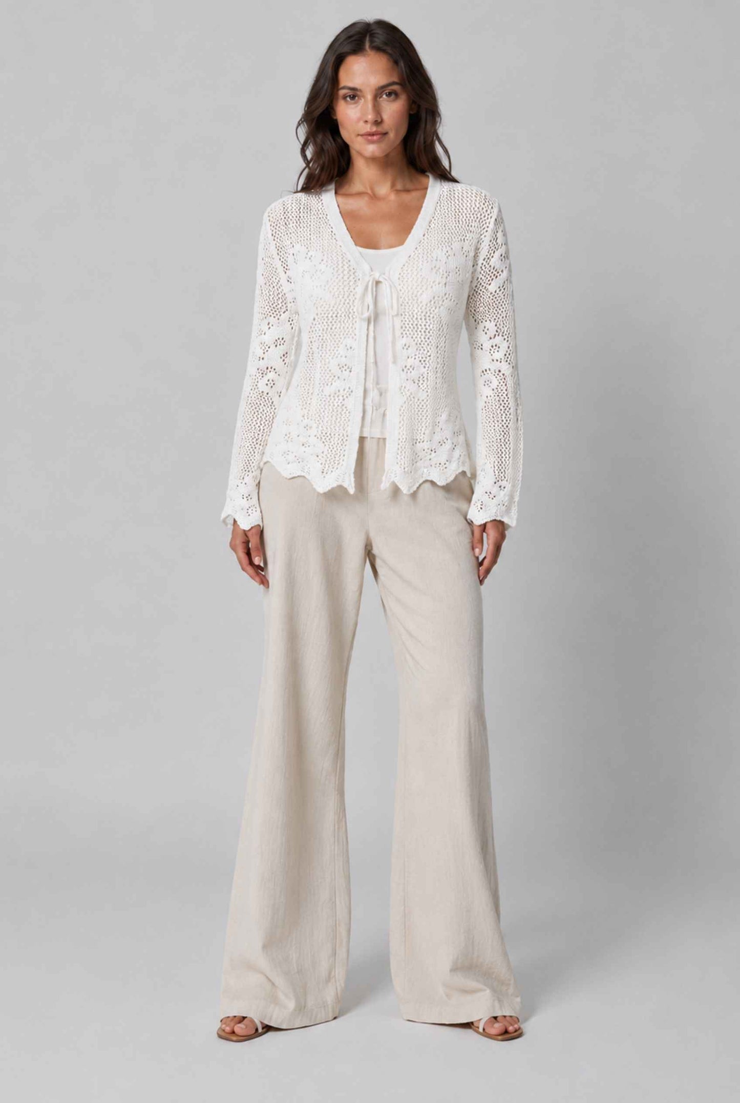 Woman wearing The Faye Tie-Front Cardigan Open Stitch White Crochet Cardigan on a gray background