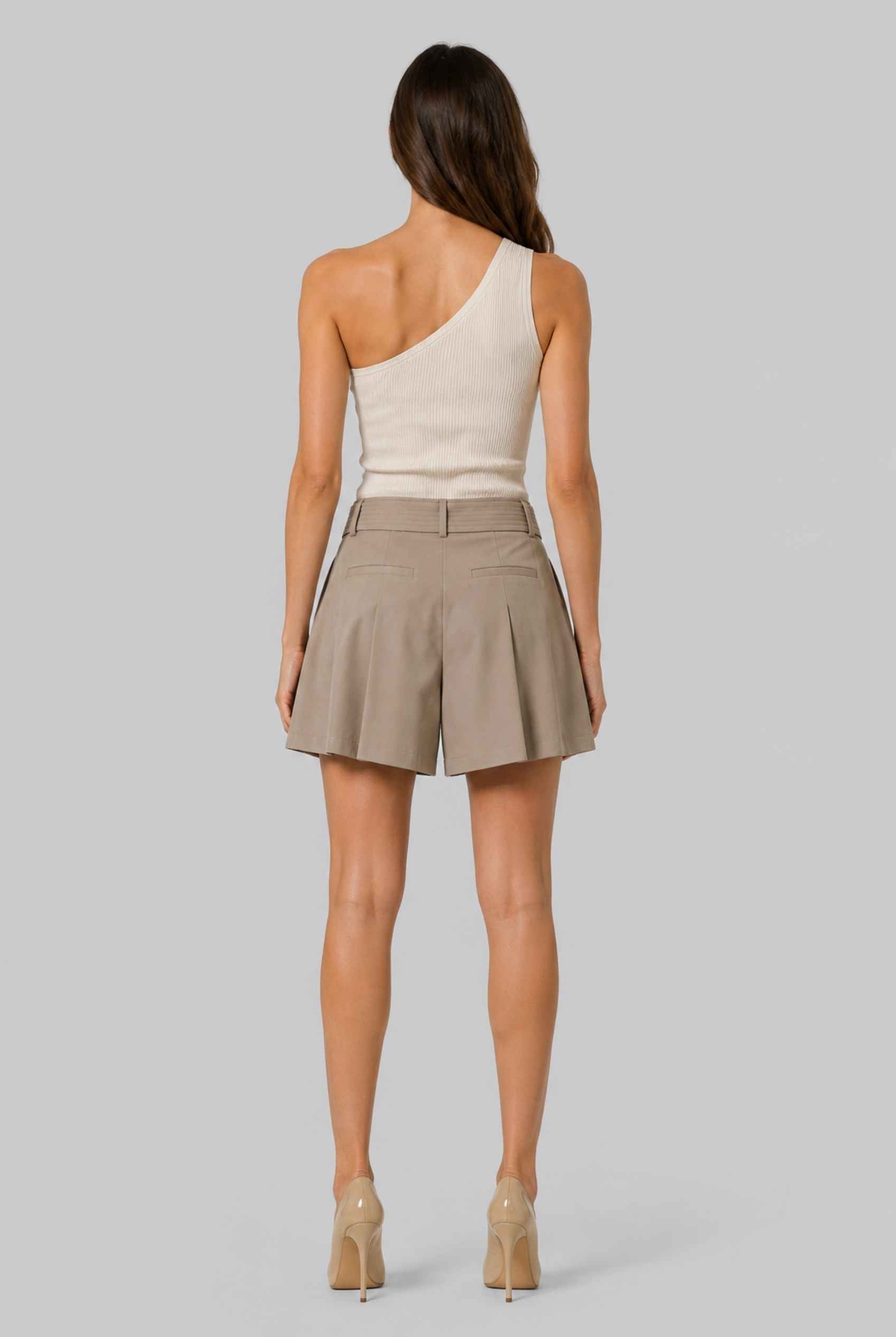 Virtual model wearing The Ottilie Pleated Short Tie-Waist Tailored Shorts in Camel with a tank top and heels on a neutral background