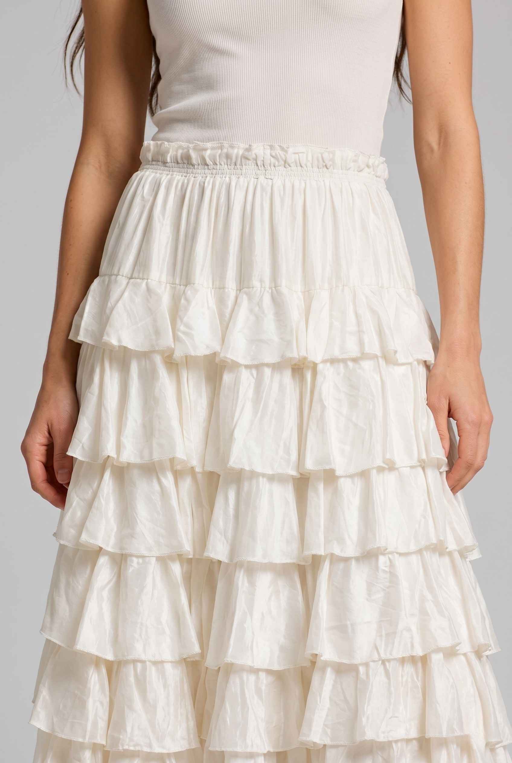 The Seraphina Tiered Skirt Ruffle Beige Midi Skirt worn by a woman on a plain background