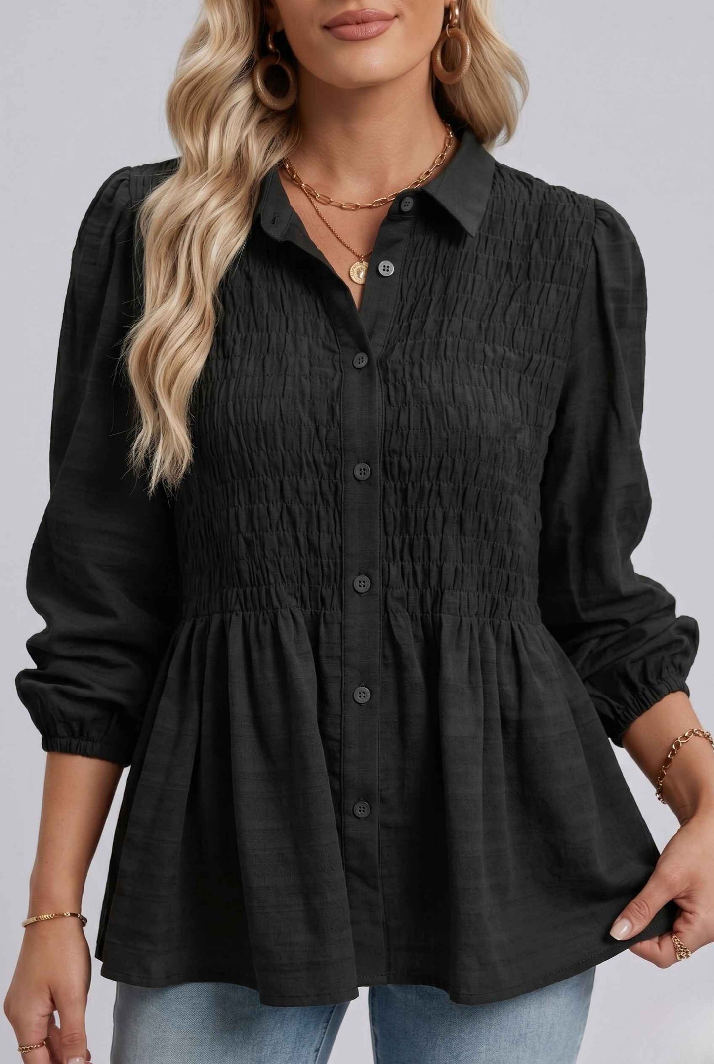Woman wearing The Sutton Peplum Blouse Smocked Button-Down Black Top with rolled-up sleeves on a plain background