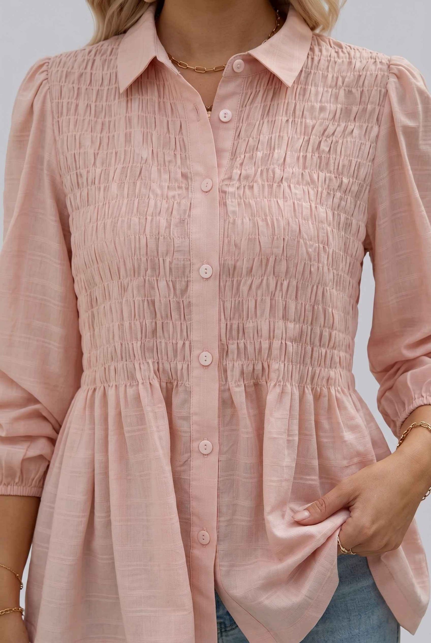 Woman wearing The Sutton Peplum Blouse Smocked Button-Down Blush Pink Top with a neutral background