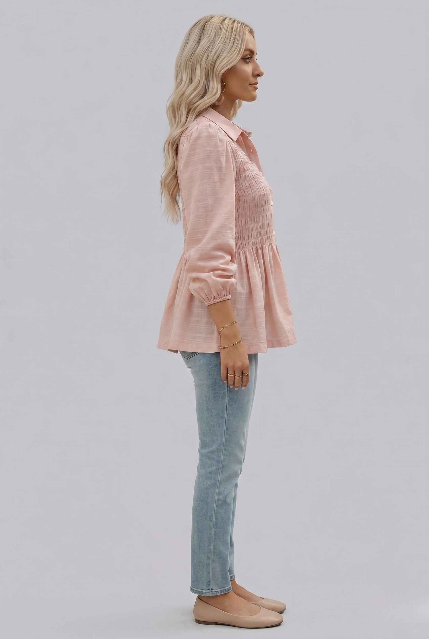 Woman wearing The Sutton Peplum Blouse Smocked Button-Down Blush Pink Top on a light gray background