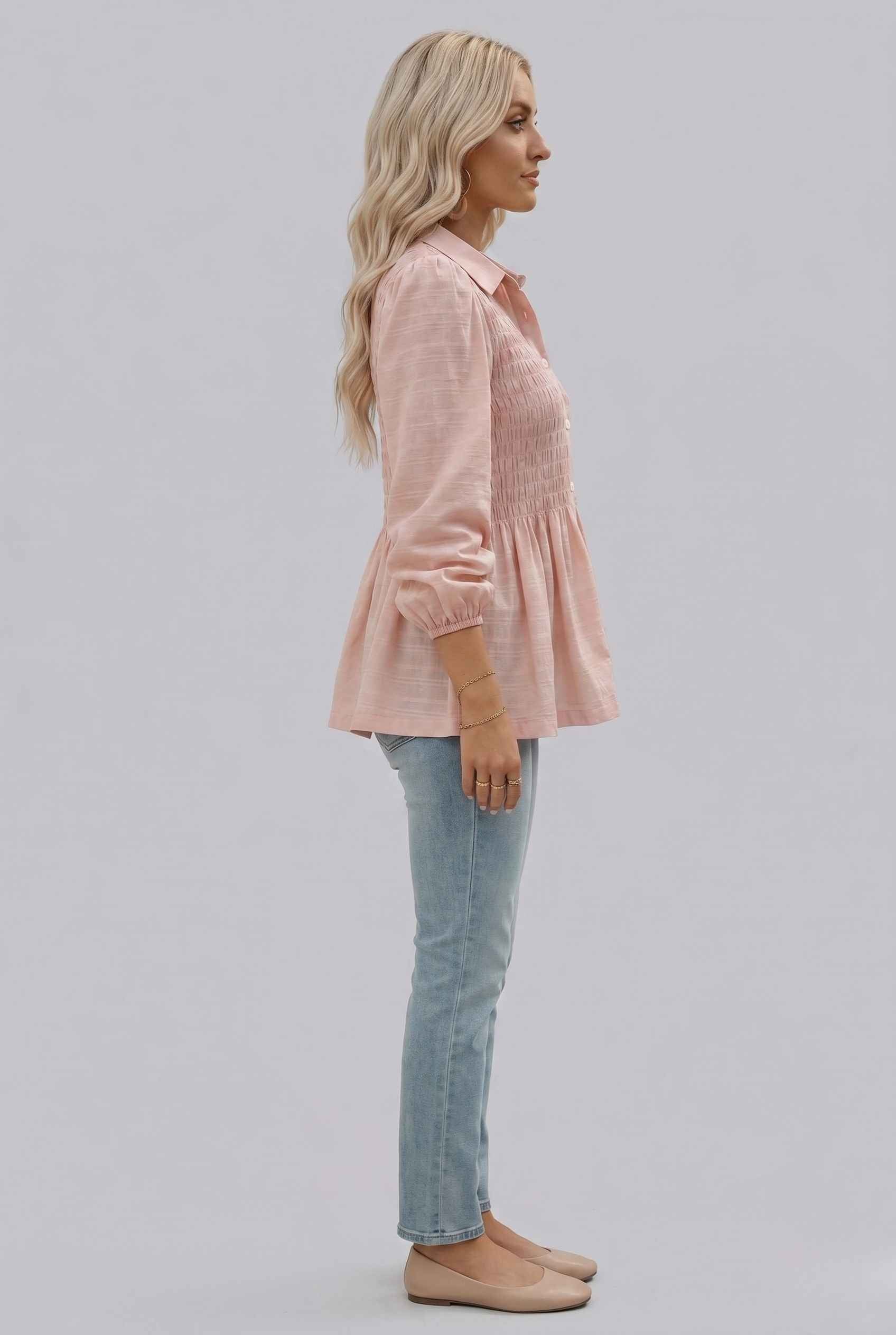 Woman wearing The Sutton Peplum Blouse Smocked Button-Down Blush Pink Top on a light gray background