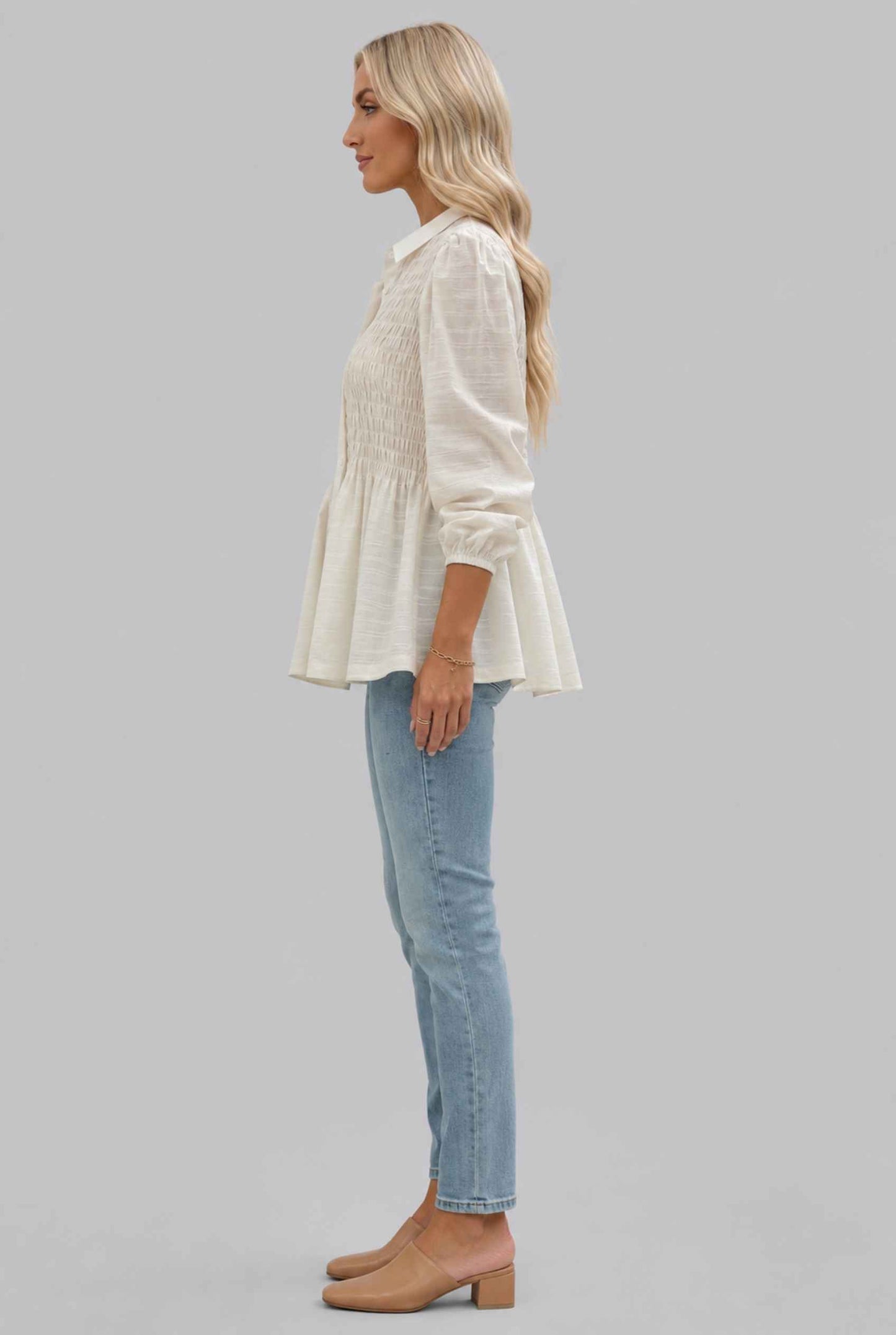 Woman wearing The Sutton Peplum Blouse Smocked Button-Down Off White Top on a gray background