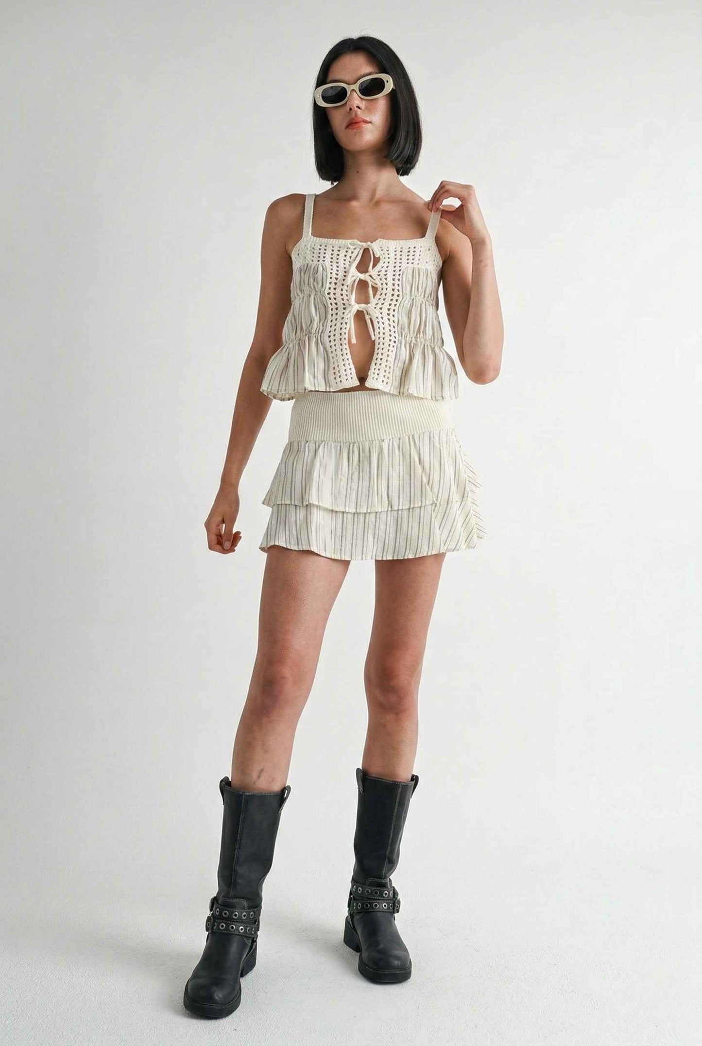 Model wearing Thea Top in Ivory Linen-Blend Peplum Cami with Pinstripes paired with matching mini skirt and tall boots on a plain background