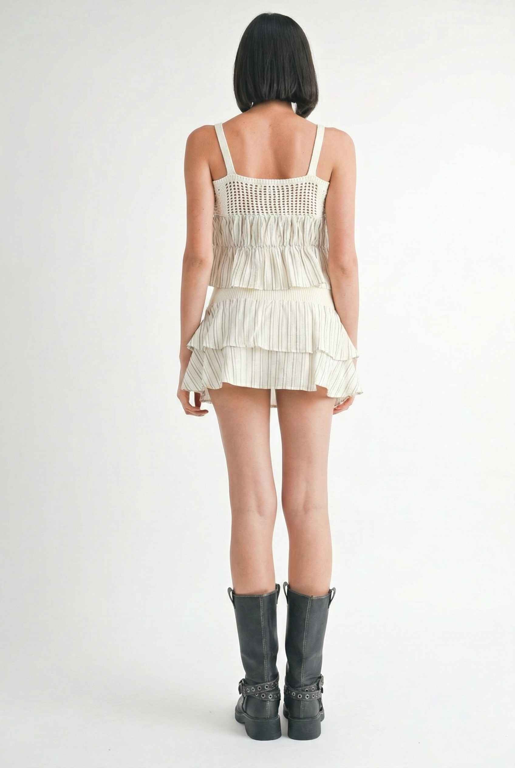 Model wearing Thea Top in Ivory Linen-Blend Peplum Cami with Pinstripes paired with matching mini skirt and tall boots on a plain background