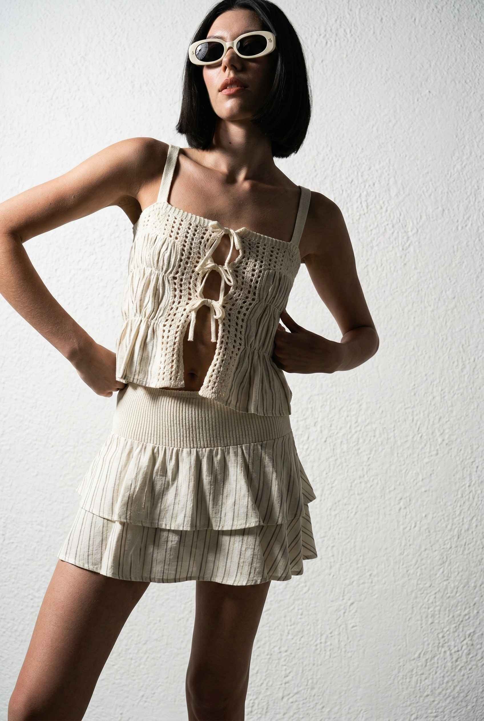Model wearing Thea Top in Ivory Linen-Blend Peplum Cami with Pinstripes paired with matching mini skirt on a plain background