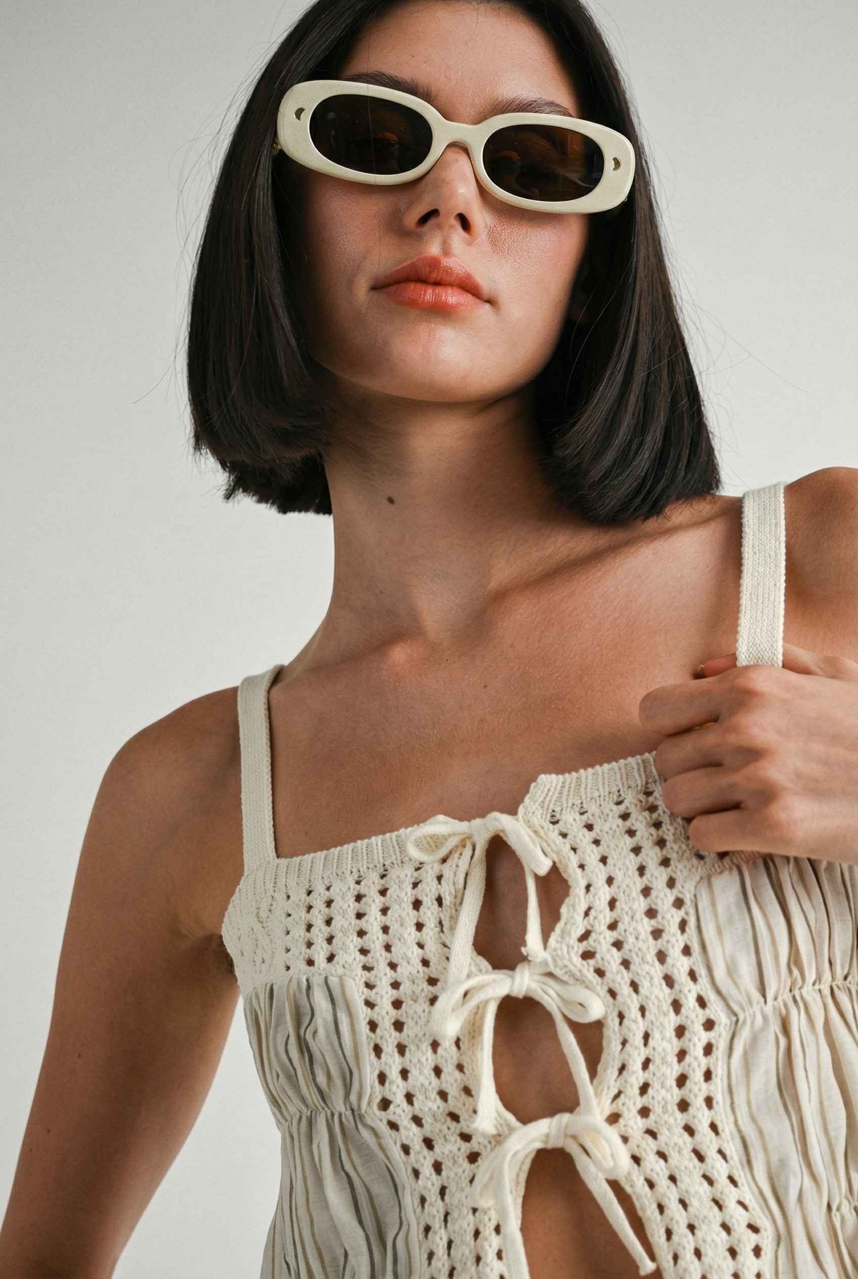 Model wearing Thea Top in Ivory Linen-Blend Peplum Cami with Pinstripes wearing sunglasses on a plain background