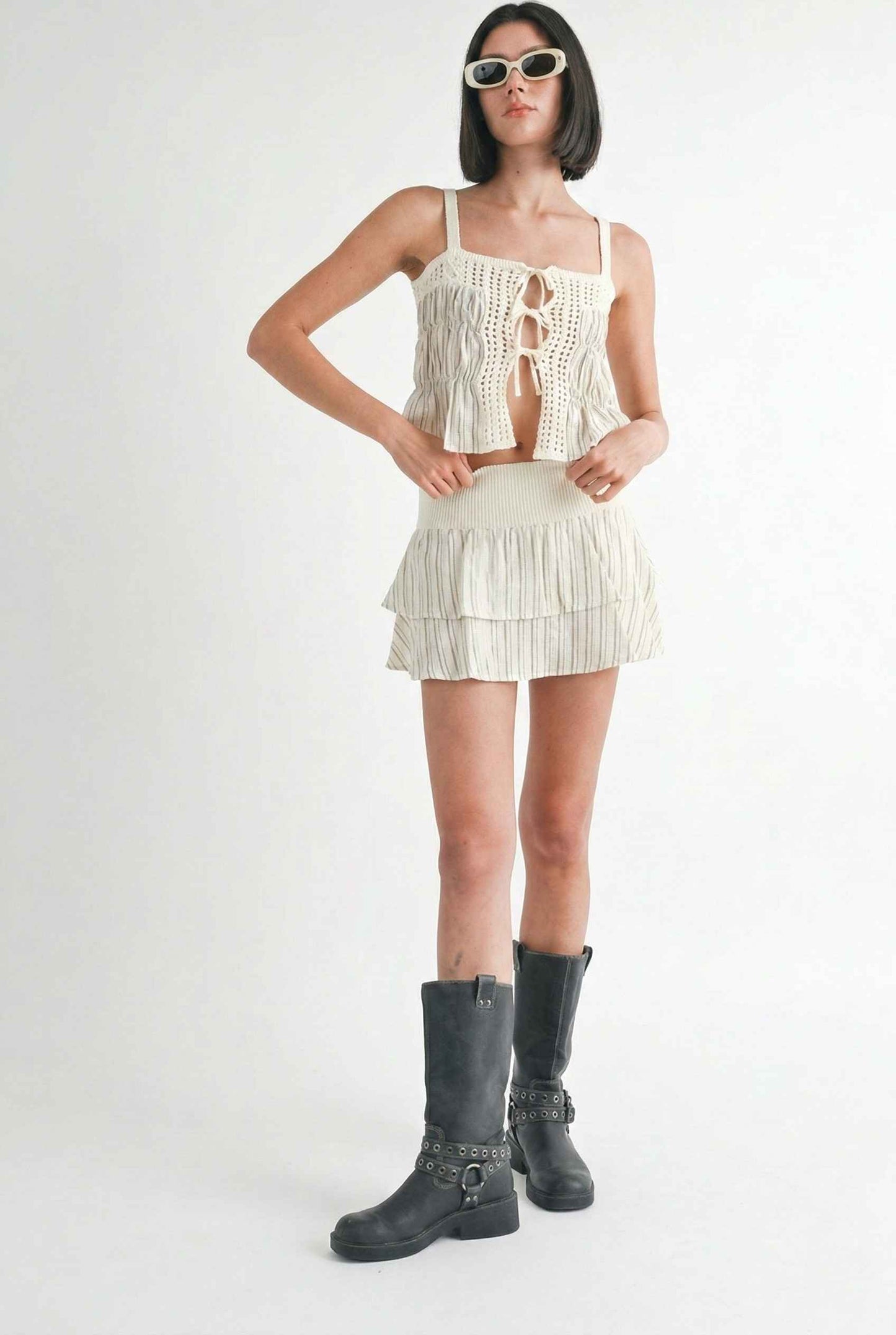 Model wearing Thea Top in Ivory Linen-Blend Peplum Cami with Pinstripes paired with matching mini skirt and tall boots on a plain background